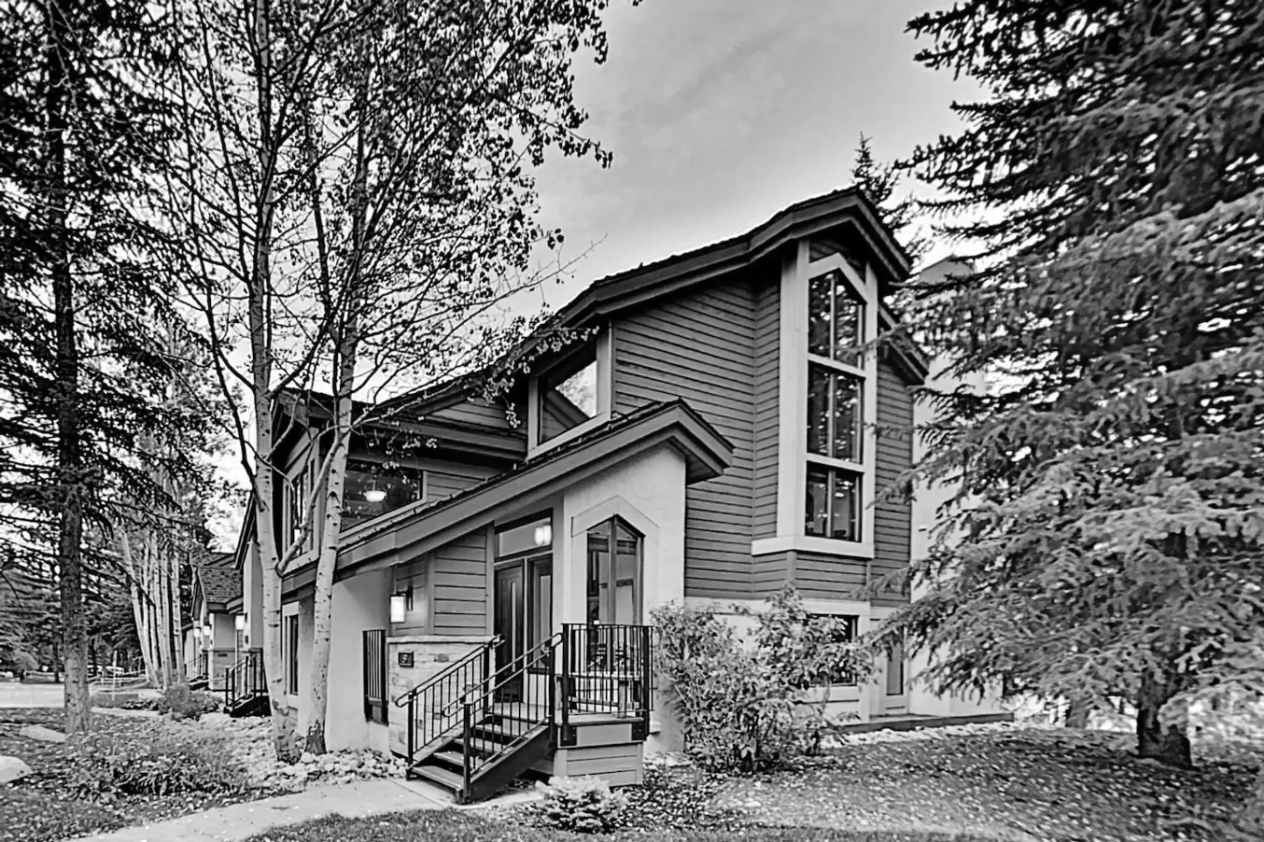 A modern multi-story house with large windows, surrounded by trees and a well-maintained yard.