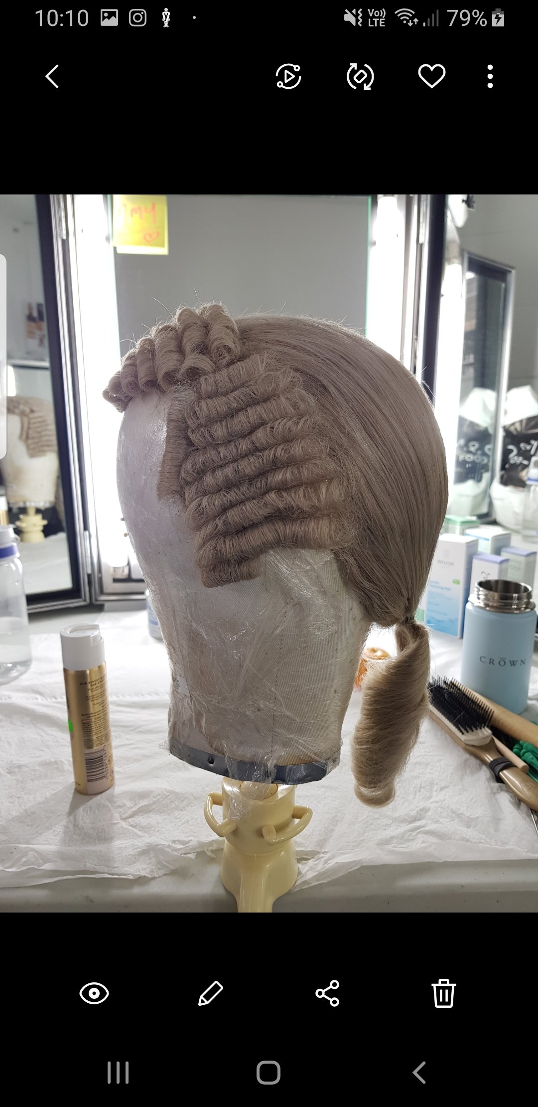Wig with intricate curls on a mannequin head, placed on a tabletop with hair styling tools.