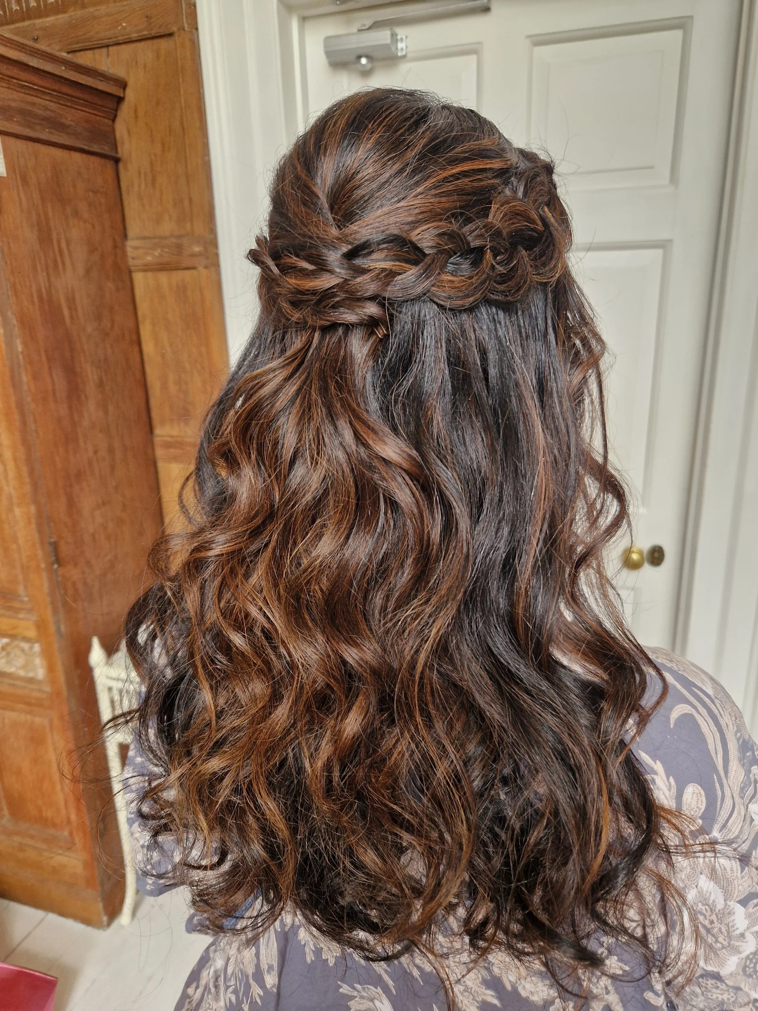 Brunette woman with long wavy hair styled in a braided half-updo.