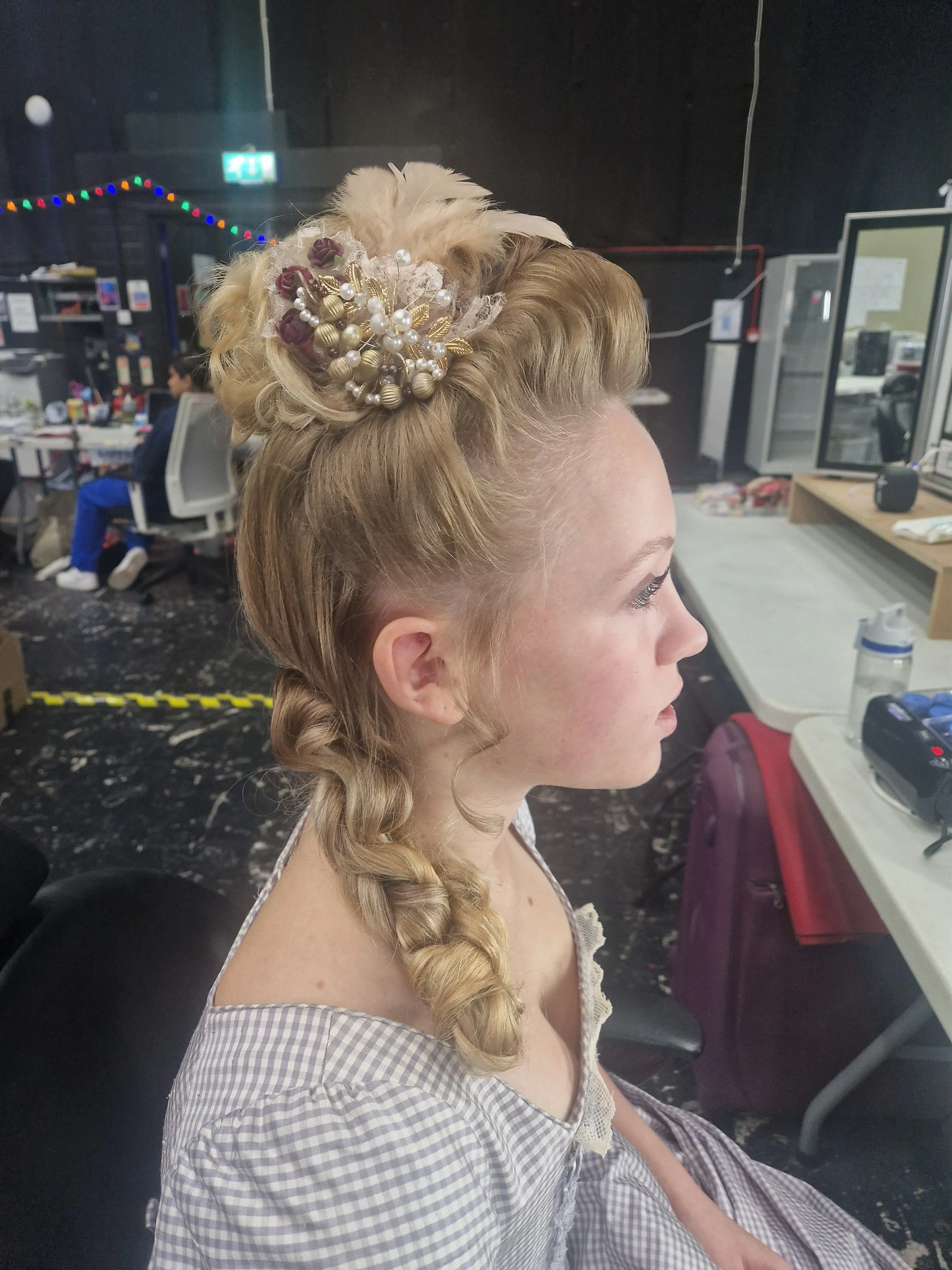 Woman with elaborate braided updo featuring decorative hairpiece sitting in dressing room