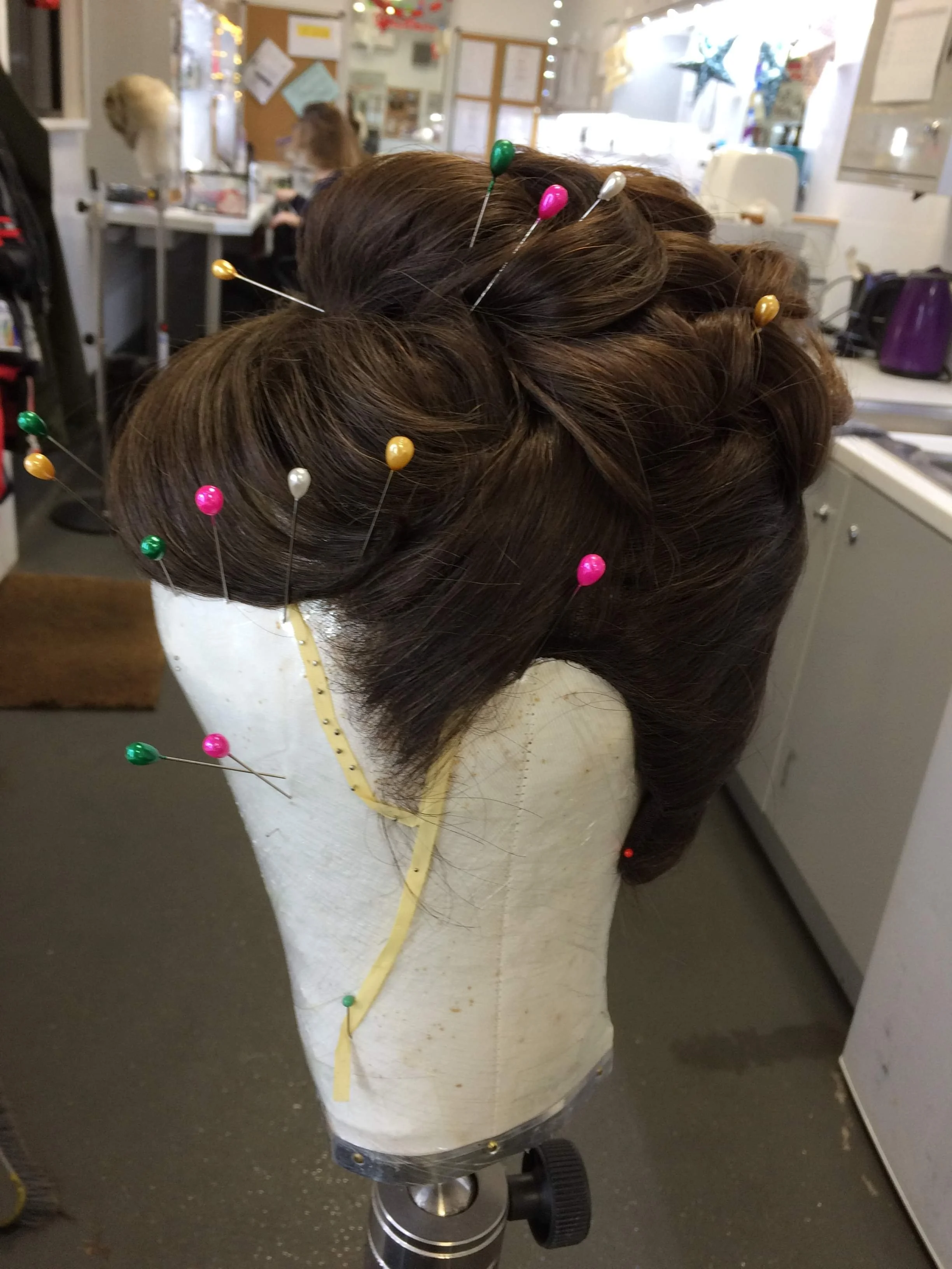 Mannequin with styled wig on stand, adorned with colorful pins, in a salon setting.