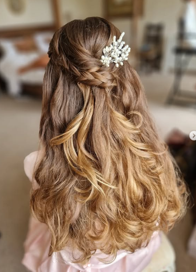 Back view of a woman with styled wavy hair, featuring a braided section and a decorative hair accessory.