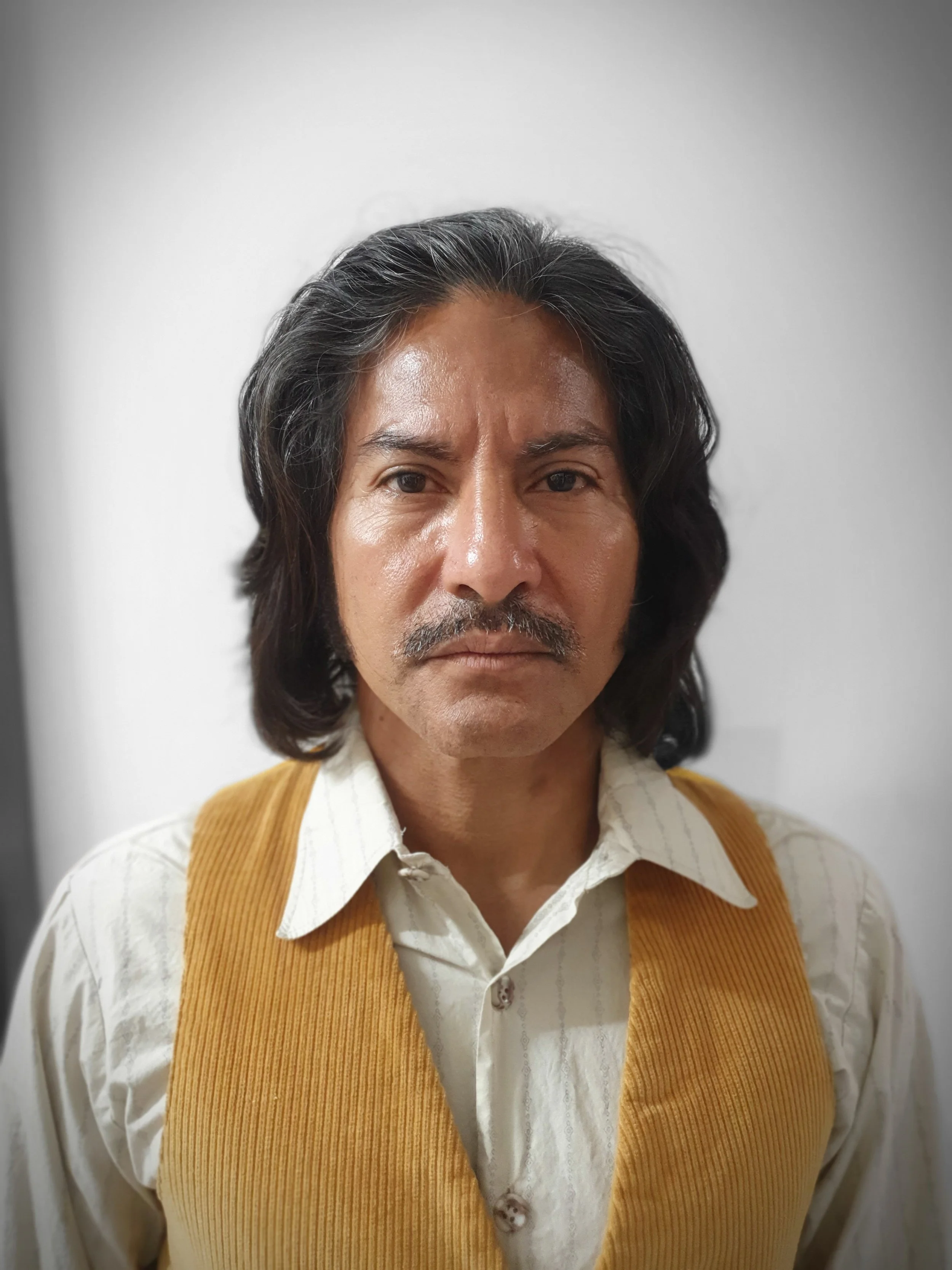 Man with long hair and mustache wearing a yellow vest and white shirt