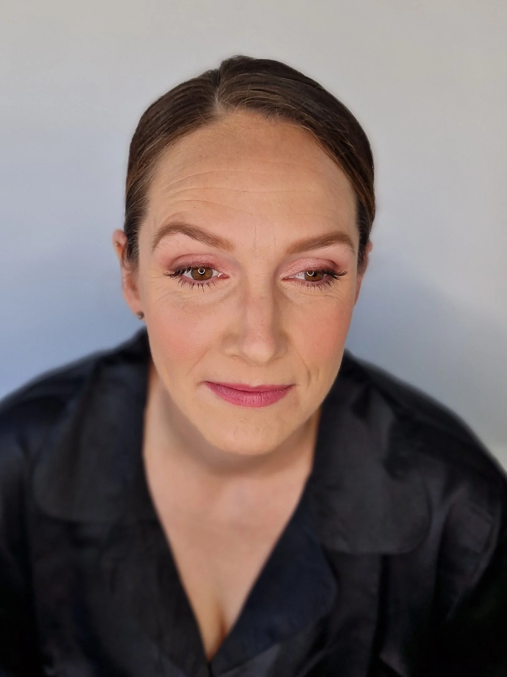 Person with slicked-back hair wearing dark clothing, looking to the side against a neutral background.