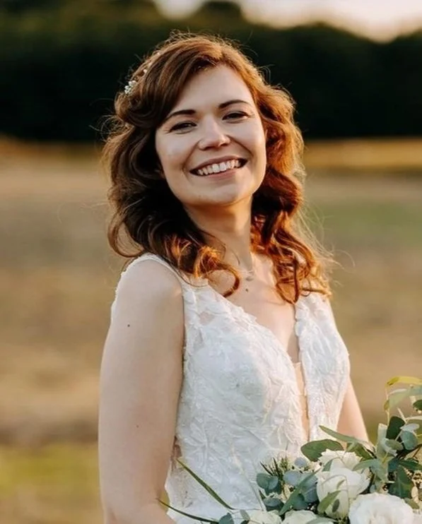 Smiling bride in white dress holding bouquet in nature setting