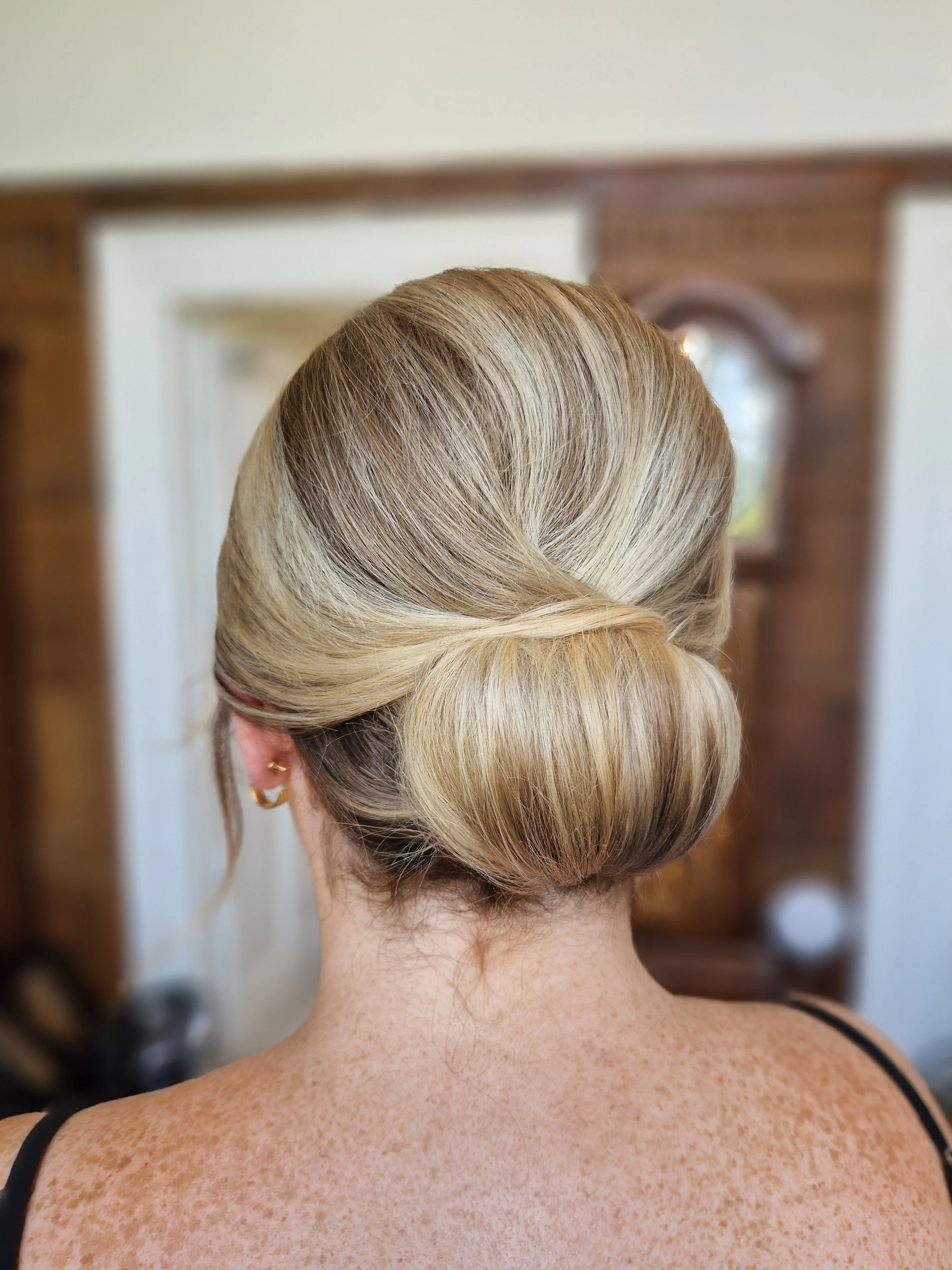 Back view of a woman with blonde hair styled in a low, elegant bun.