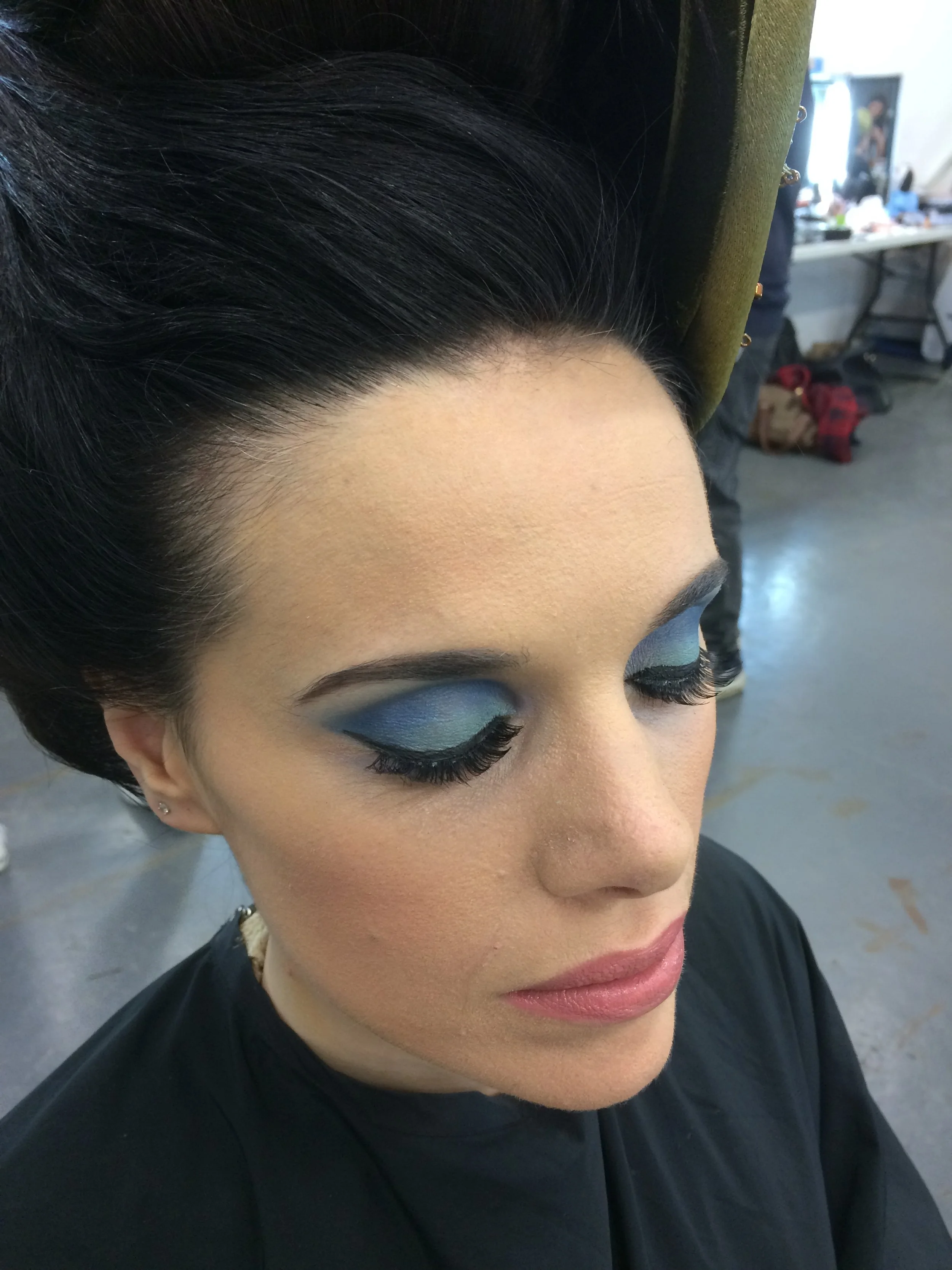Woman with dramatic blue eye makeup and styled dark hair in a salon.