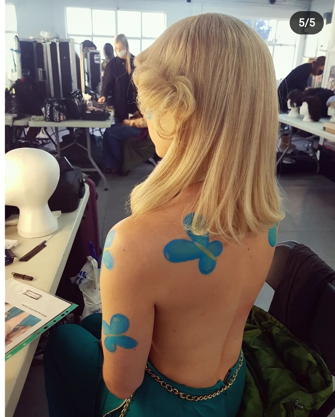Person with blue body paint backstage at photoshoot.