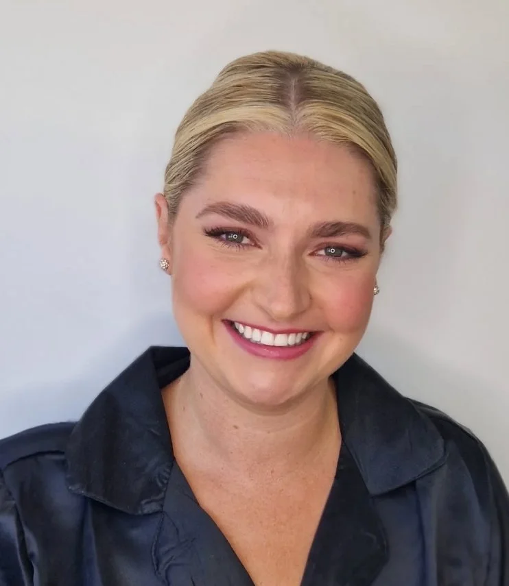 Smiling woman with blonde hair in a bun, wearing a black jacket.