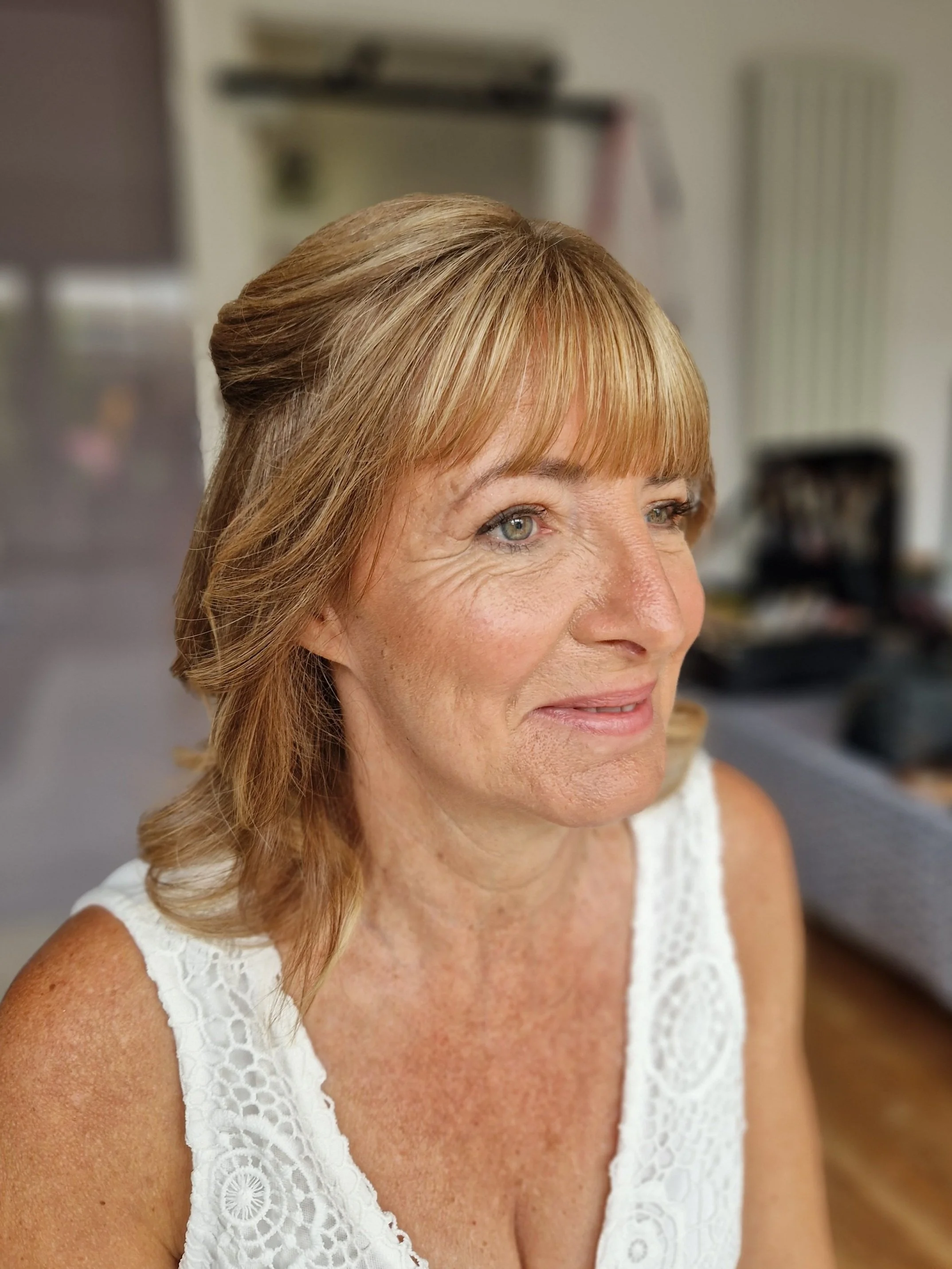 Portrait of a smiling woman with blonde hair and a white lace top, indoors.