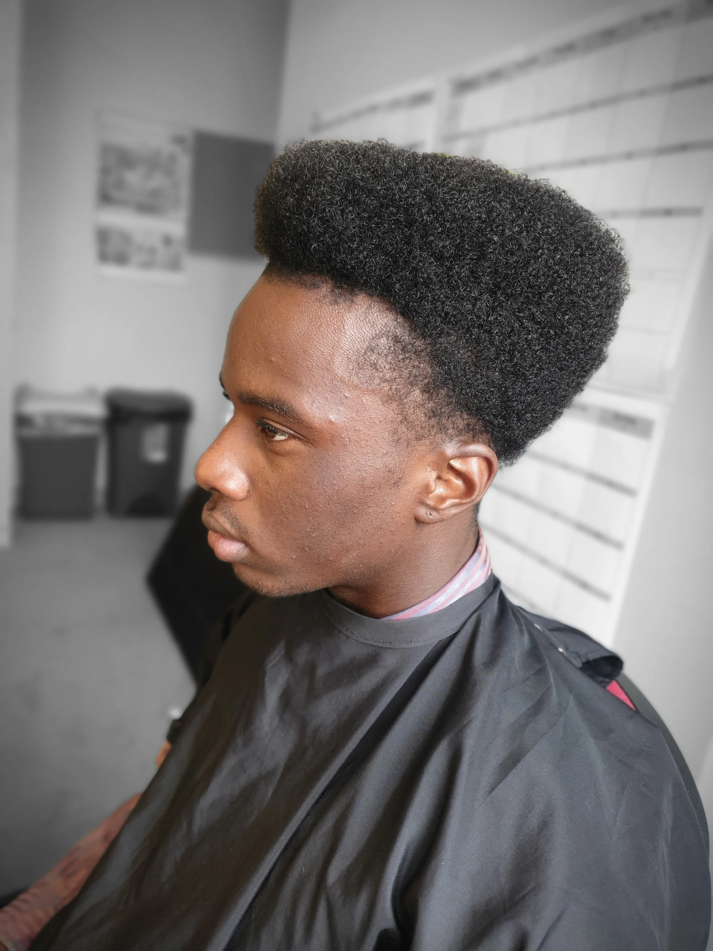 Person with a high-top fade hairstyle sitting in a room with a calendar on the wall in the background.