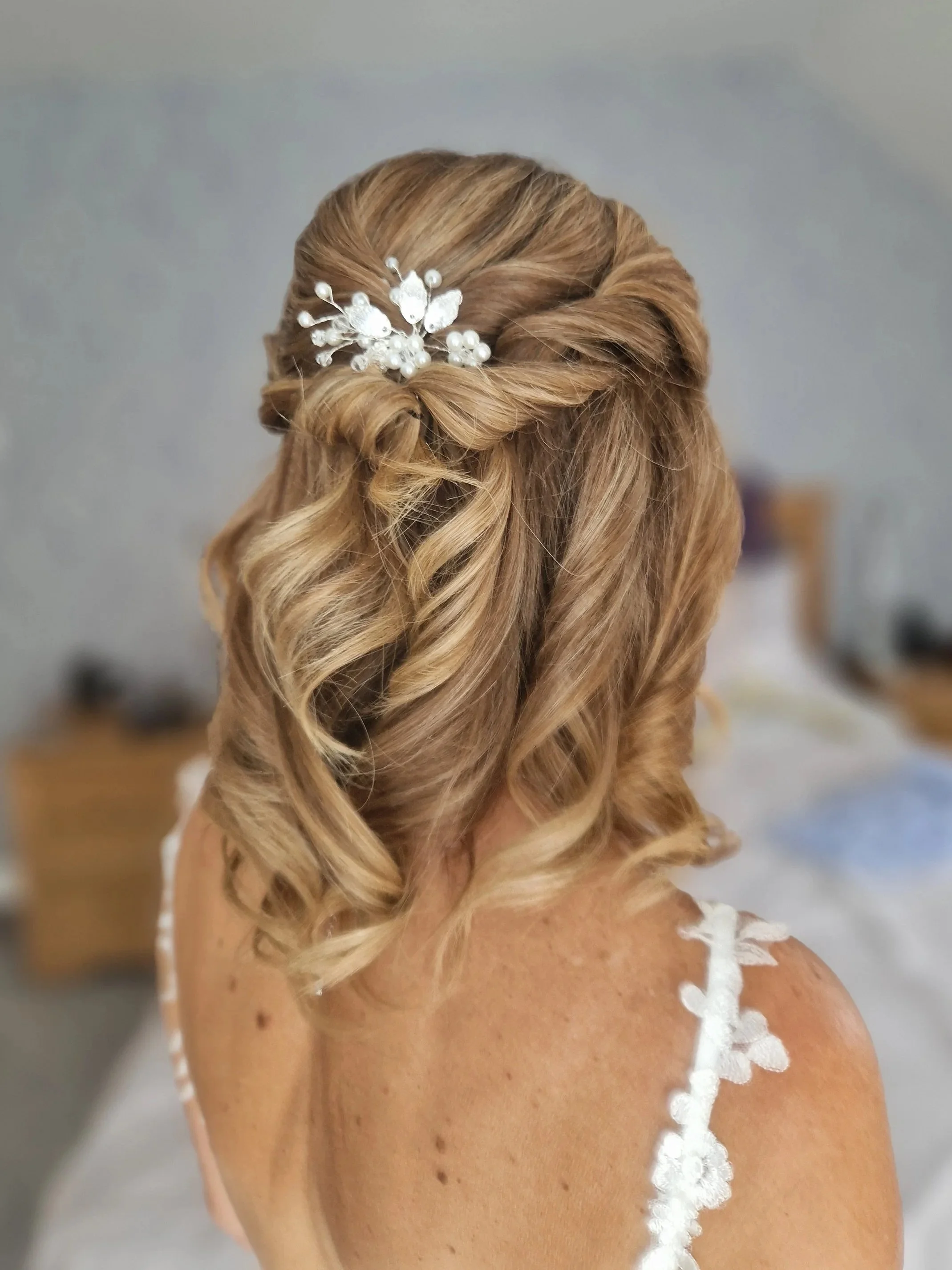 Woman with styled curly hair and floral hair accessory, wearing a white dress with floral straps.