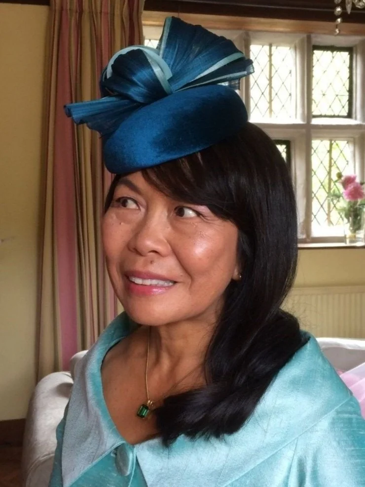 Woman wearing a blue fascinator and outfit, smiling indoors.