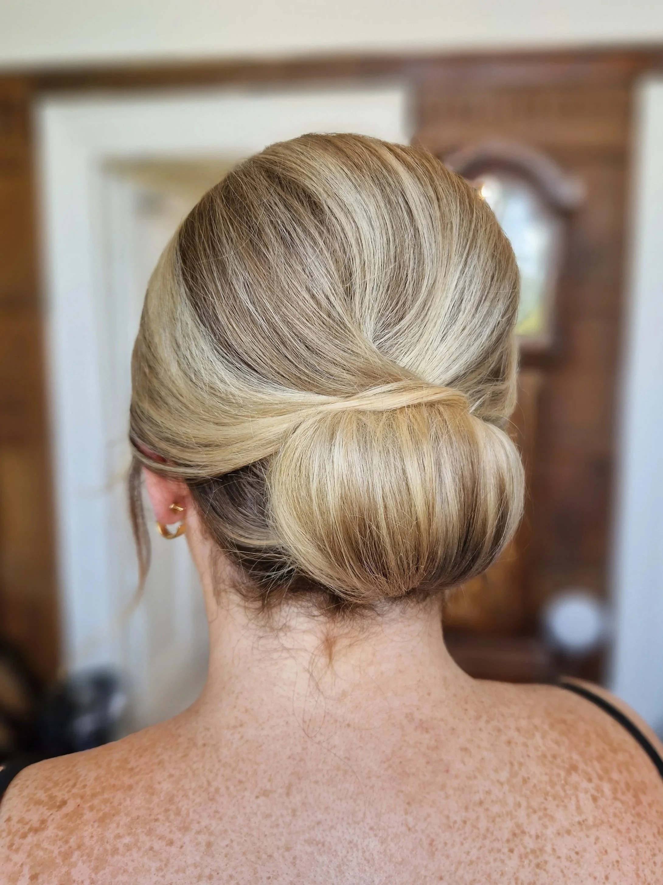 Back view of a woman with blonde hair styled in a low, elegant bun.