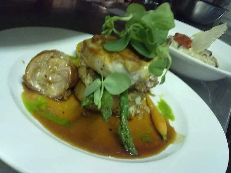 Gourmet dish with grilled chicken breast, asparagus, and microgreens on a white plate with sauce.