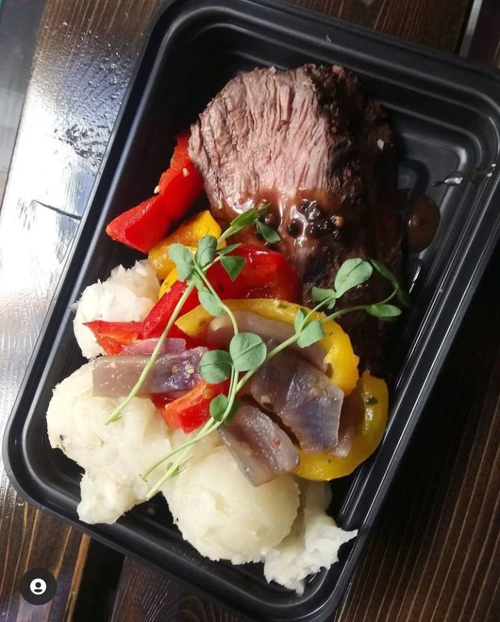 Black container with Prime Rib, colorful bell peppers, Yucca mash, and microgreens.
