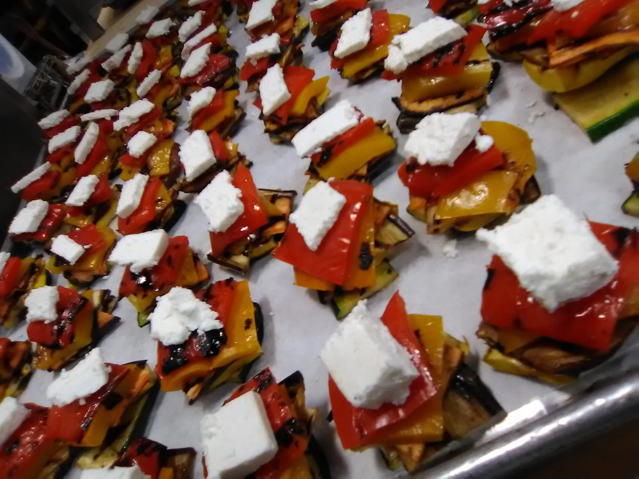 Appetizers with grilled vegetables, red and yellow bell peppers, and feta cheese cubes on a tray.