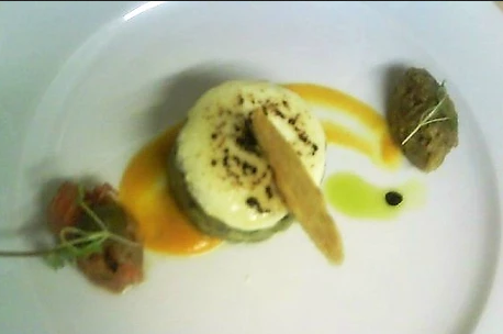 Gourmet dish with layered vegetable stack, cheese topping, sauce drizzle, and garnished with microgreens on a white plate.