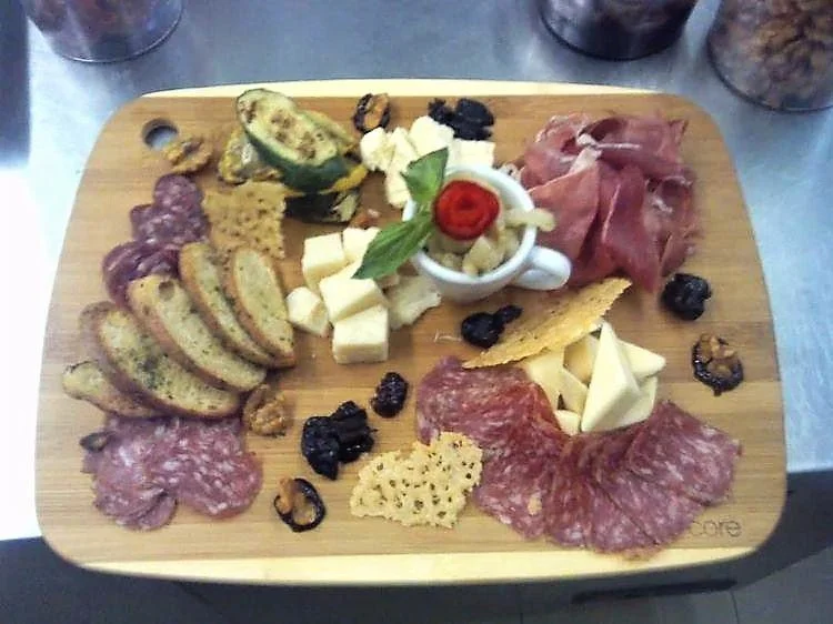 Charcuterie board with assorted cheeses, cured meats, crackers, sliced bread, fruit, and garnishes on a wooden platter.