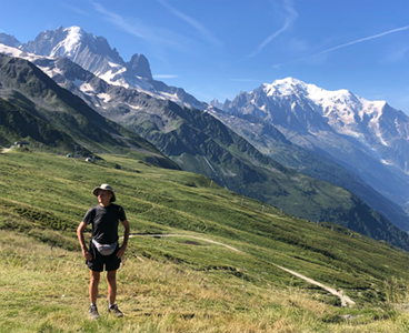 Dan Miller standing on a grassy hillside with snow-capped mountains in the background on a clear, sunny day.