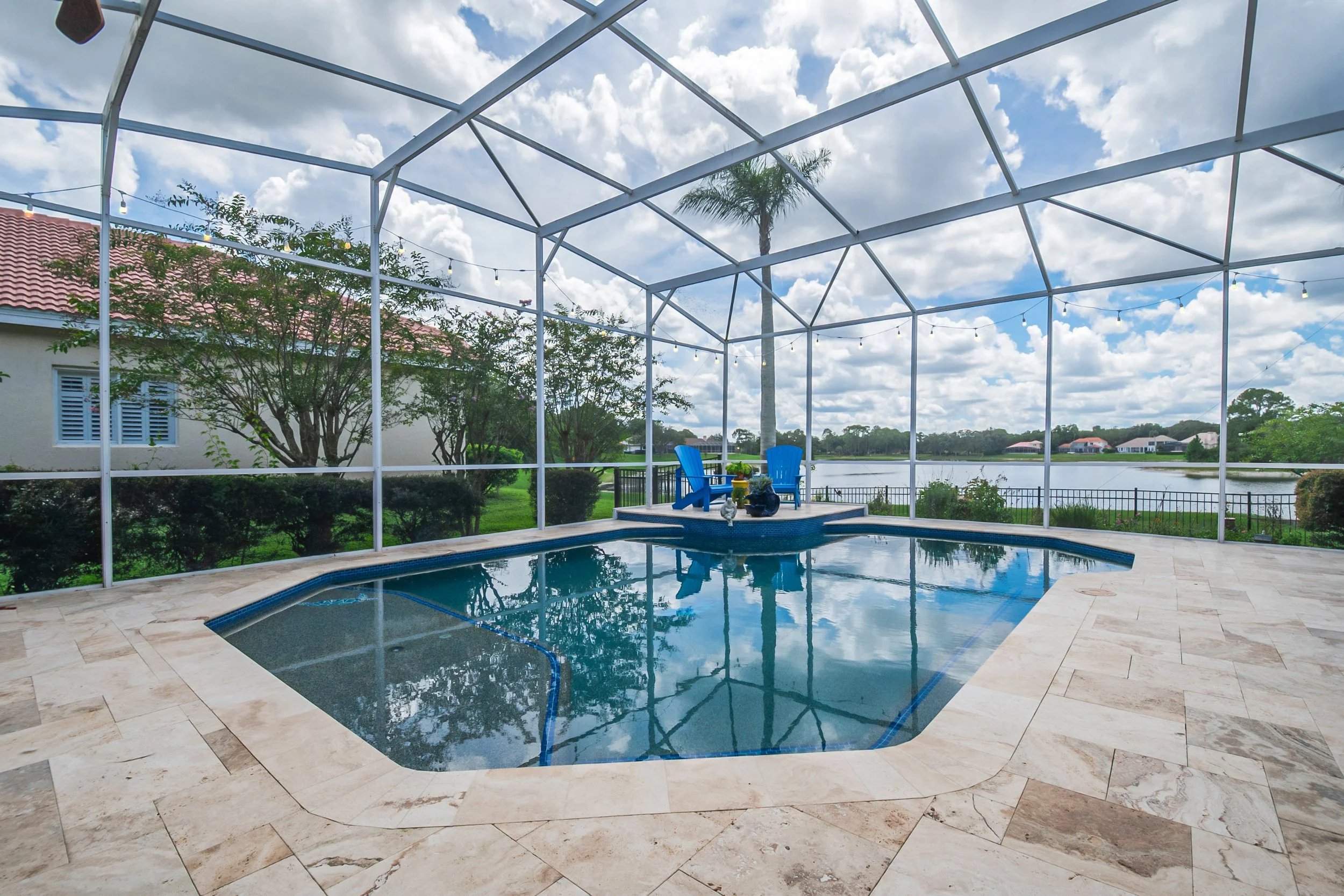 Enclosed backyard swimming pool area with a screen, with luxurious glass tiles, overlooking a lake and greenery.