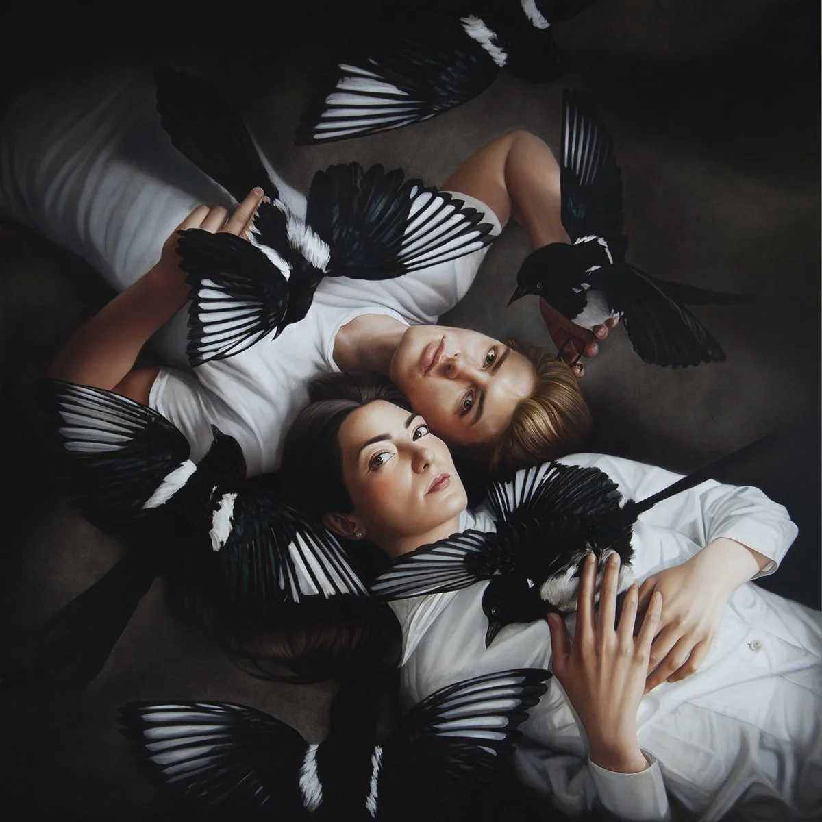 Two women lying on a bed surrounded by black and white butterflies, gazing at the camera.