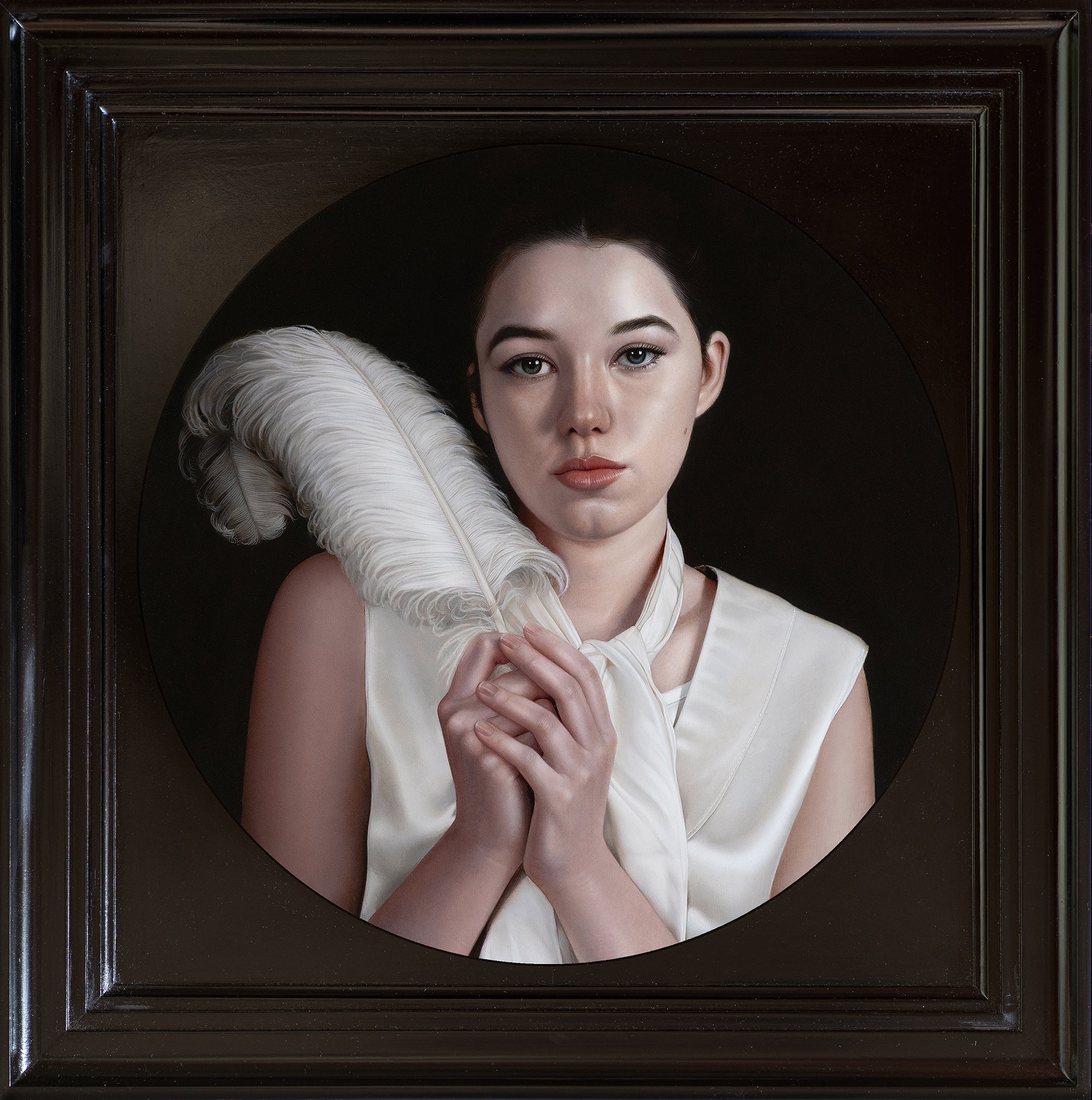 A woman with fair skin and dark hair, holding a large white feather, wearing a white sleeveless dress and a white scarf around her neck, in a black-framed square portrait with a sealed black background.
