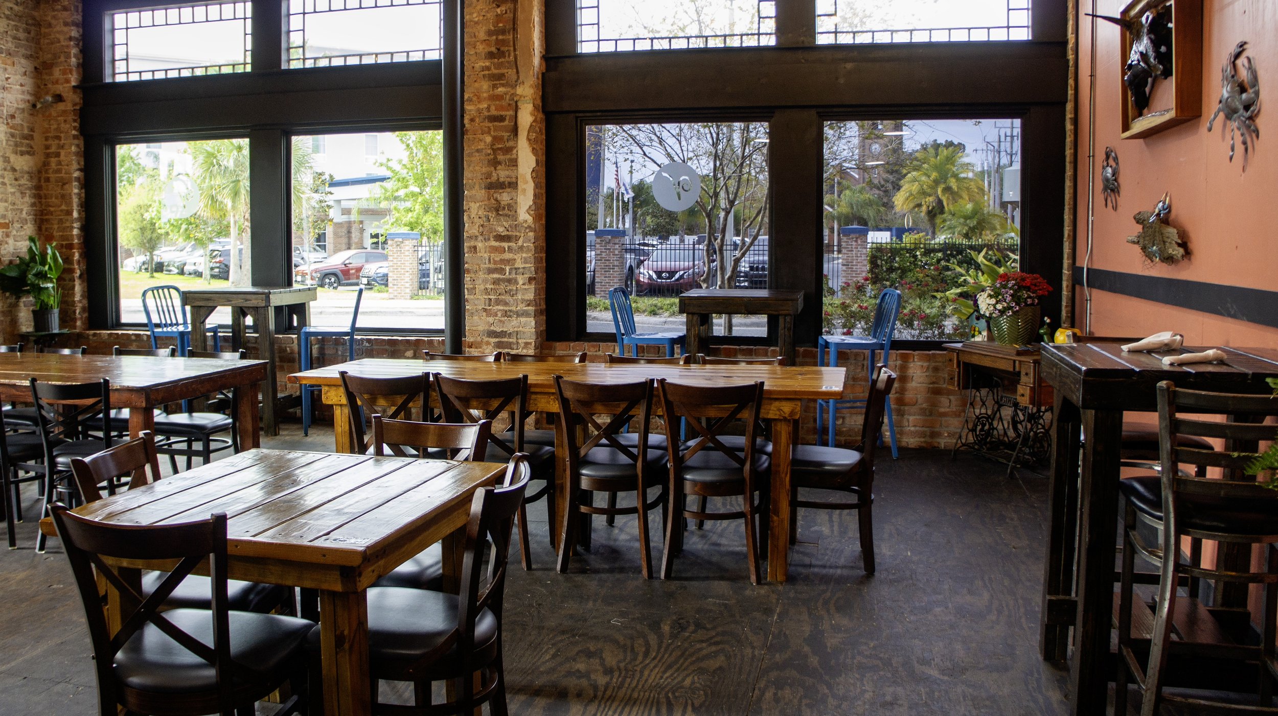 Interior of a cozy restaurant with wooden tables and chairs, large windows, brick walls, and wall decorations featuring sea motifs.