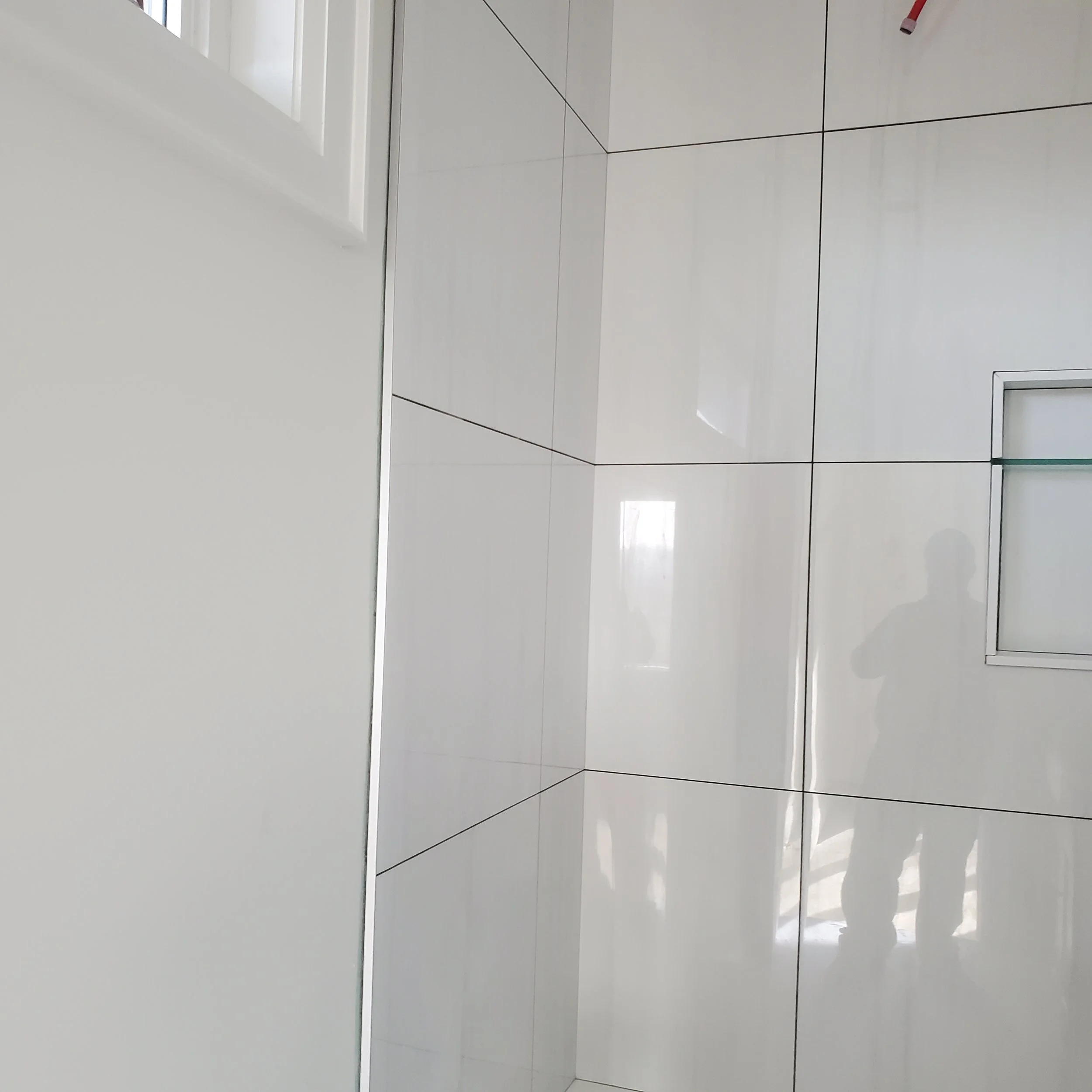 A tiled corner of a bathroom with glossy white tiles and a small built-in shelf.
