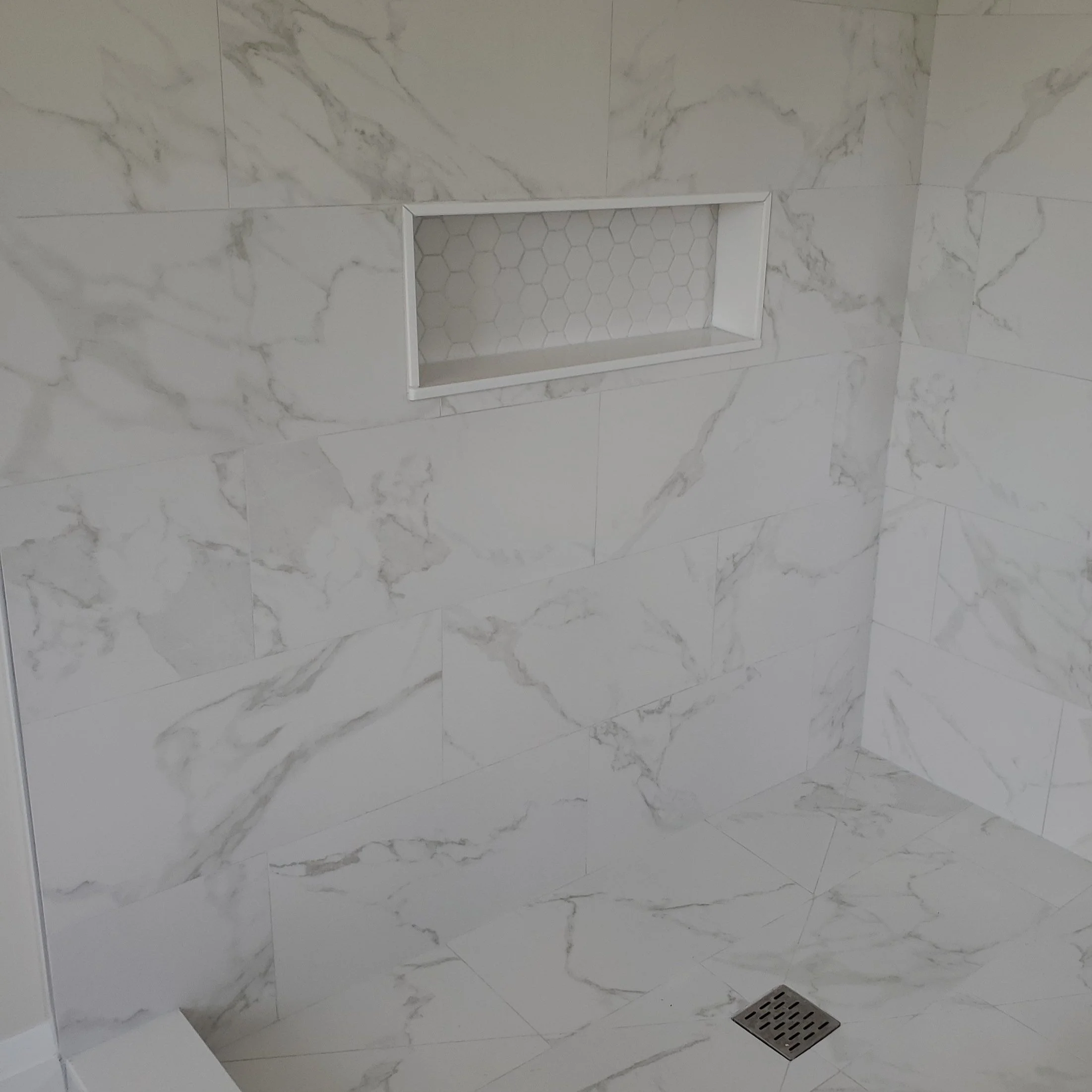 Bathroom shower wall with white marble tiles and built-in shelf, featuring hexagonal tile design inside the niche.