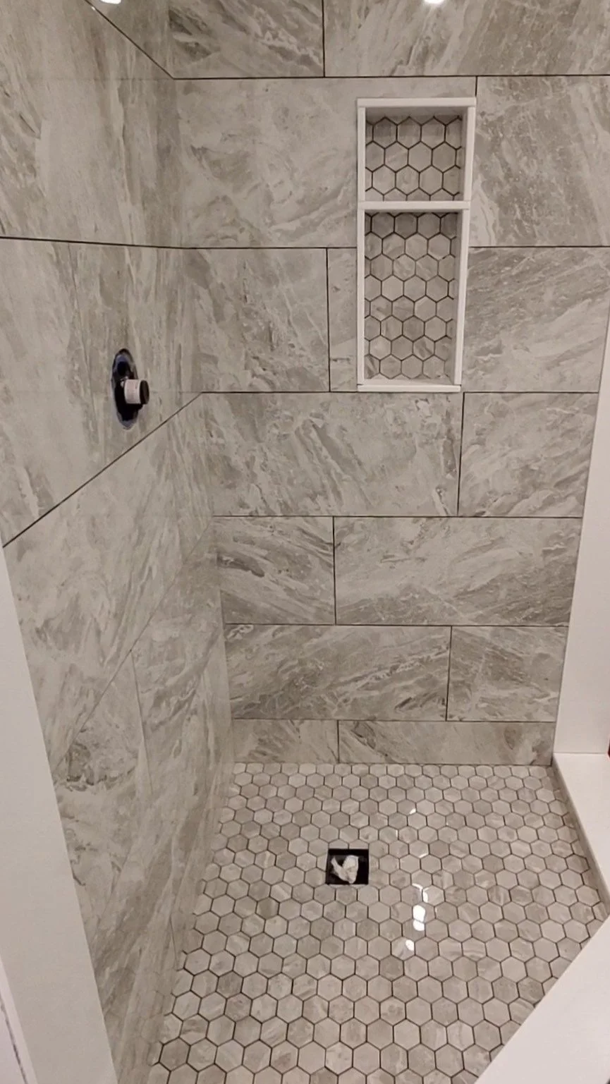 Modern shower with gray marble tiles, hexagonal floor tiles, and a wall niche.