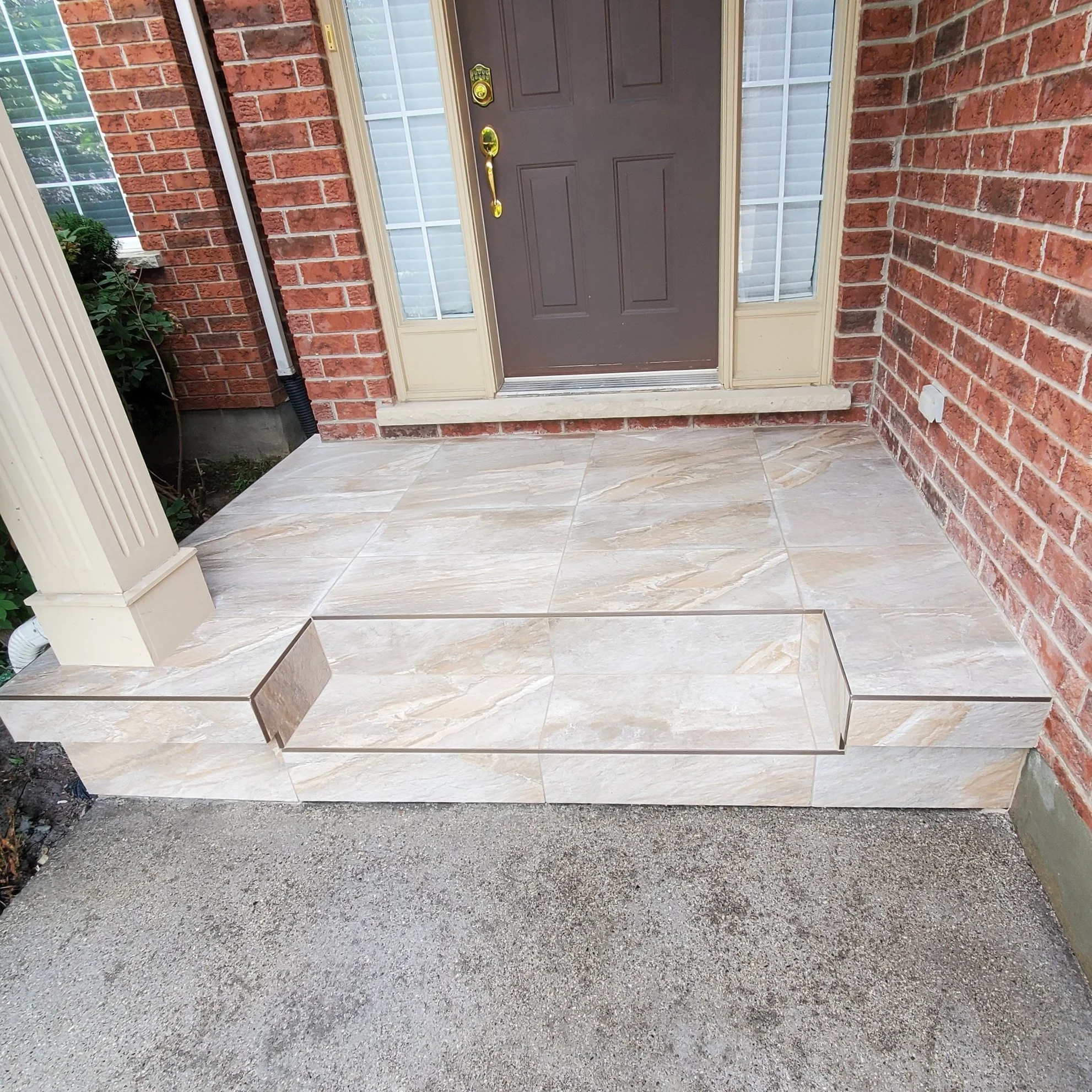 Front entrance of a house with beige tiled steps, red brick walls, and a brown door with brass hardware.