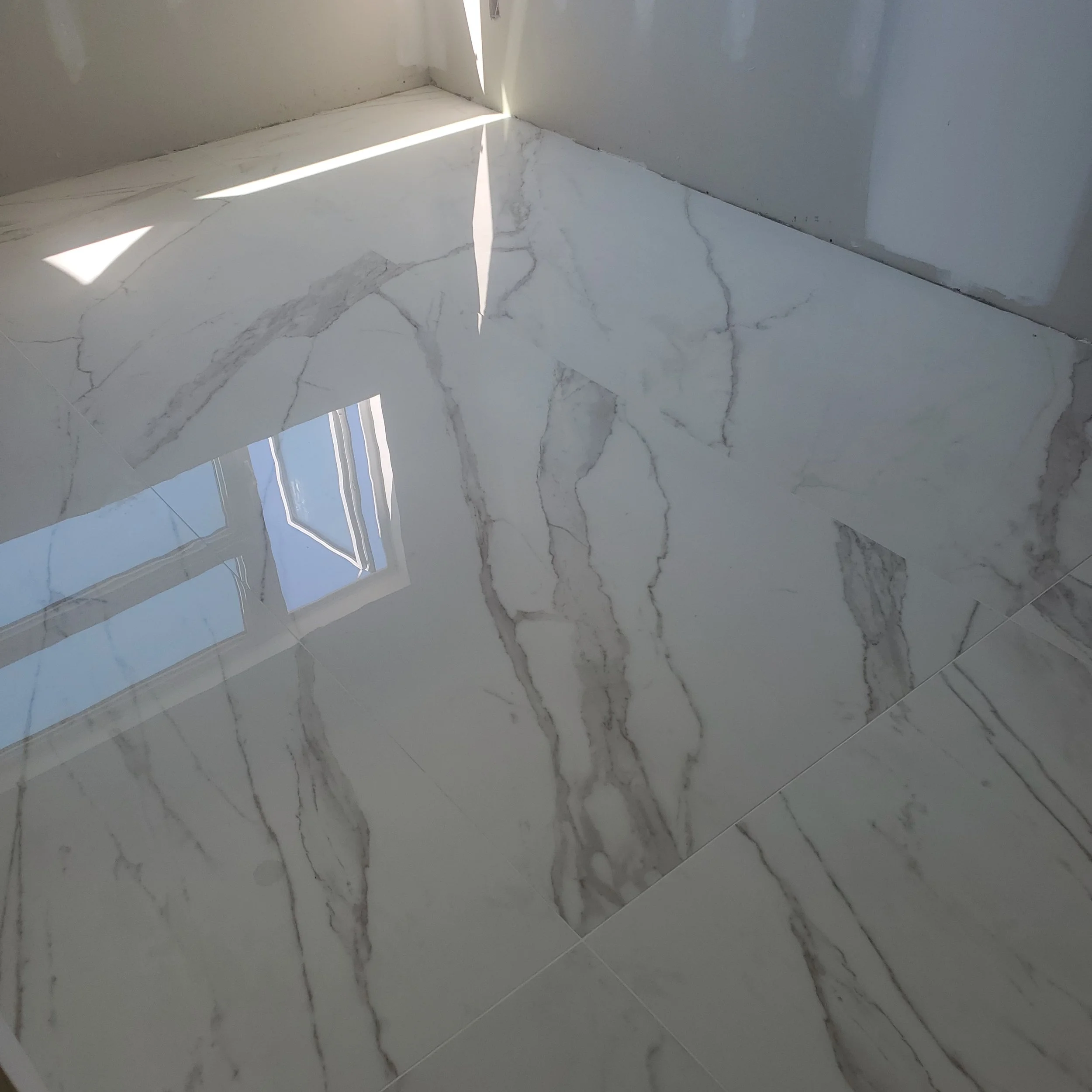 Polished white marble floor tiles with gray veining reflecting light from a window.