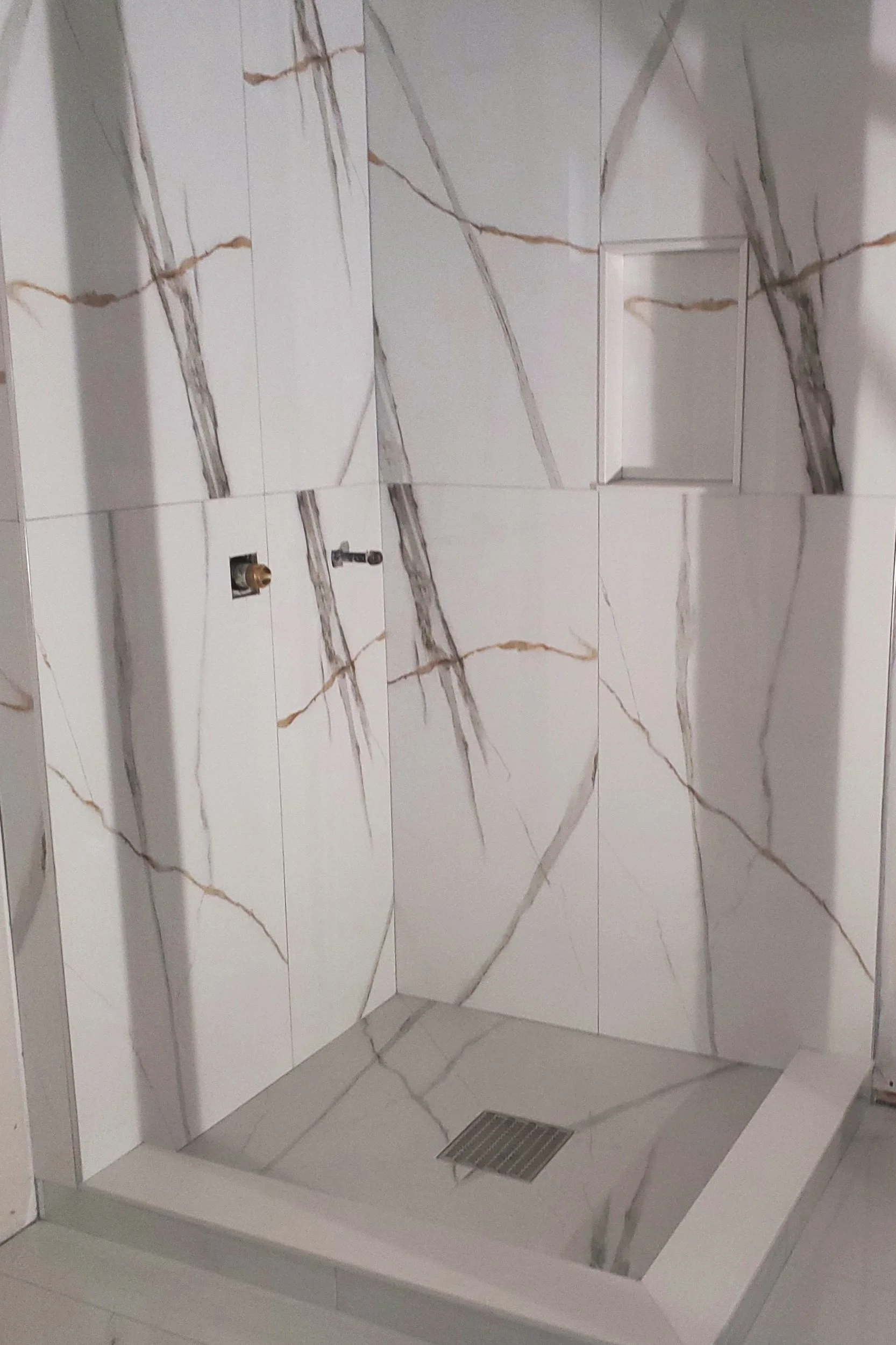 Modern bathroom shower with marble tile, featuring brown and gray veining, and a built-in niche.