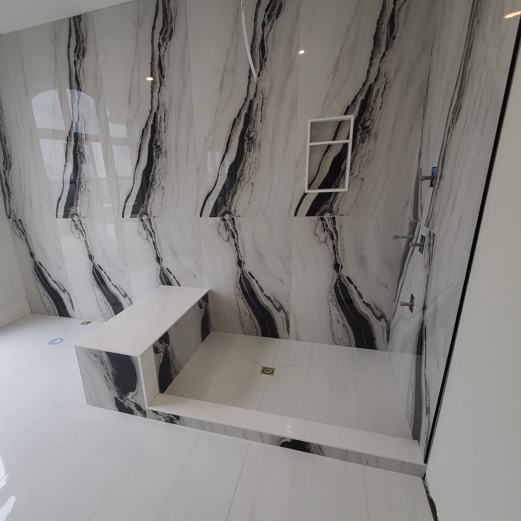 Modern shower with marble-patterned tile walls and a built-in bench