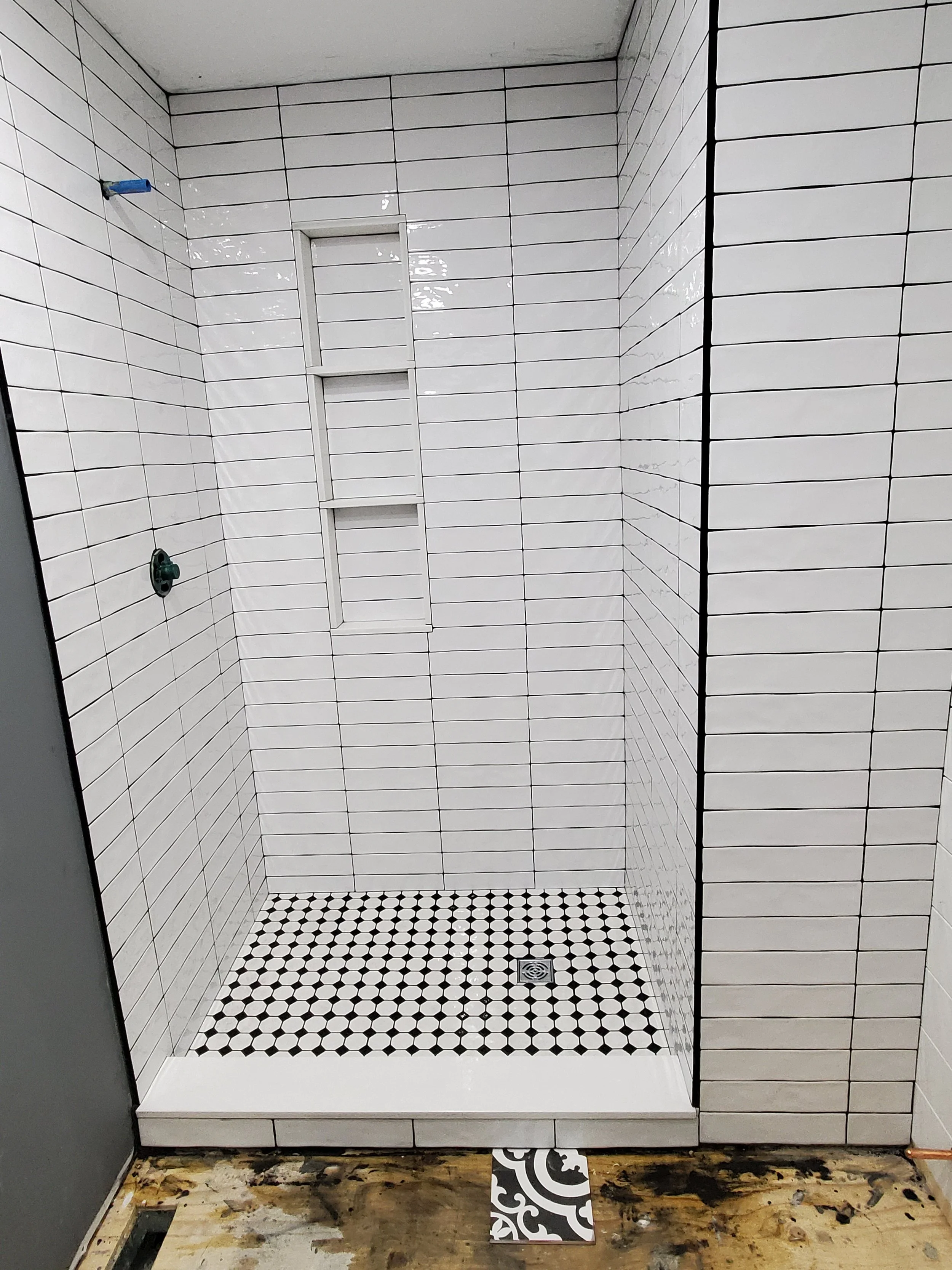 Newly tiled shower with white subway tile walls and a black and white patterned floor.