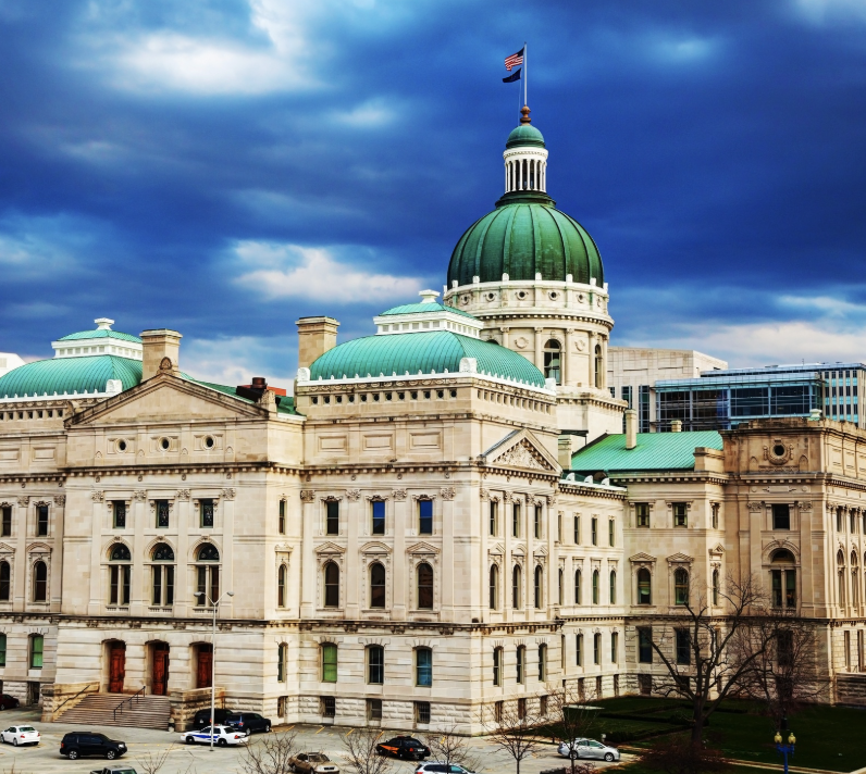 Capitol building with green domes and a flag under a dark, cloudy sky.
