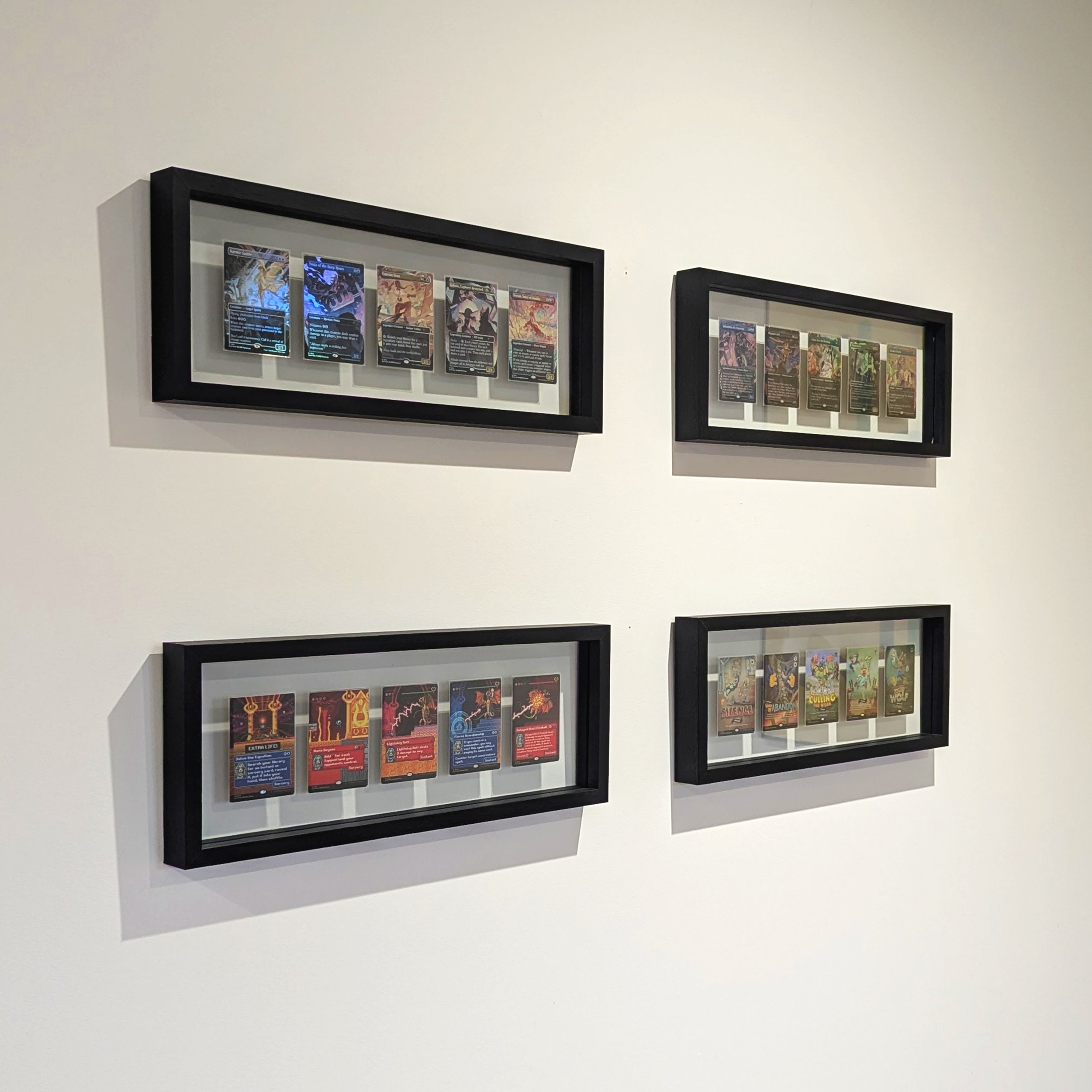 Quatre cadres noirs contenant des cartes de jeu affichées au mur, organisés en deux rangées et deux colonnes.
