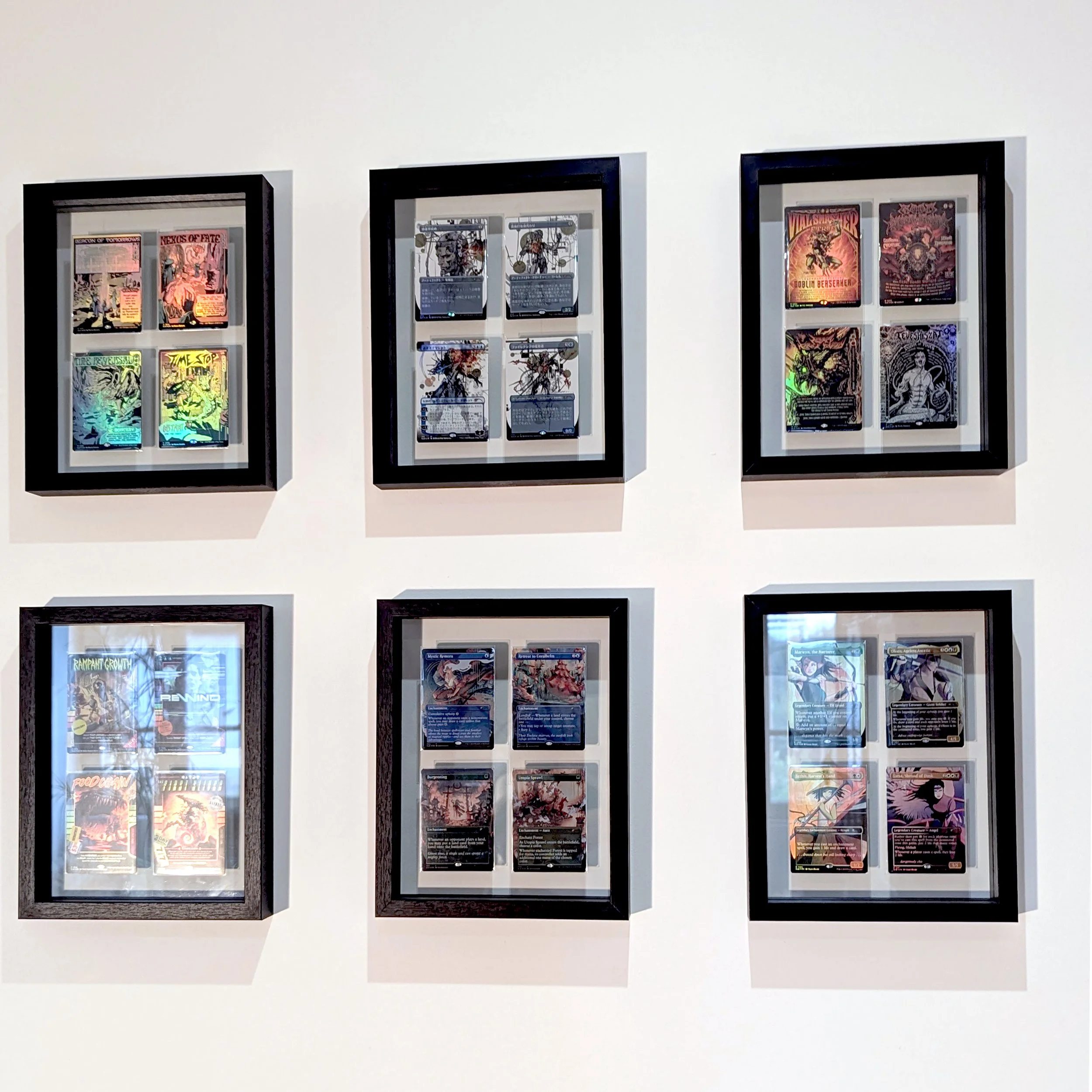 Exposition de six cadres muraux contenant des cartes de jeux de cartes à collectionner, avec différentes illustrations et textes.