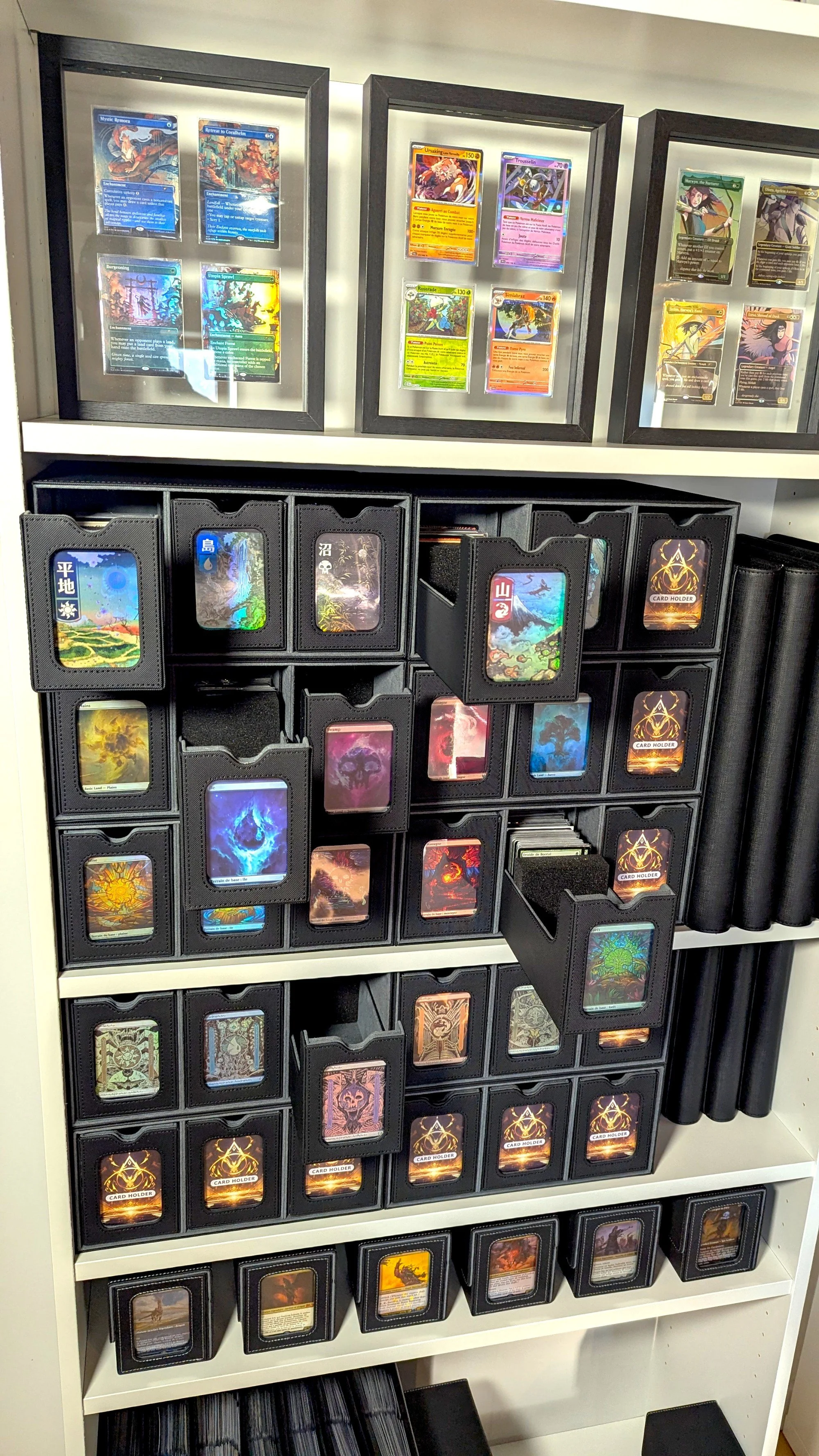 Une collection de cartes de jeu, avec des cartes encadrées en haut et des cartes dans des boîtiers noirs organiquement rangés dans une armoire.