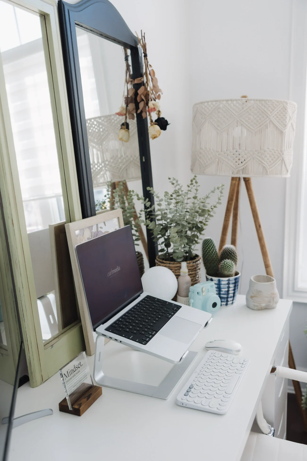 A white desk setup with a MacBook and greenery/decor.