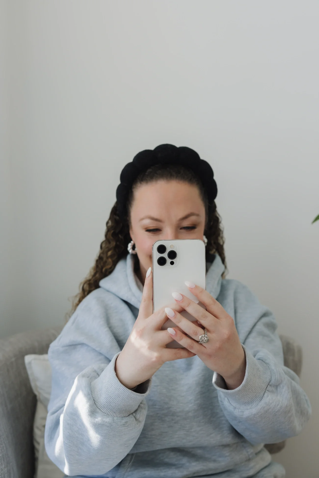 Cassie of Curl Media taking a selfie with her iPhone, wearing a gray hoodie and a black headband.