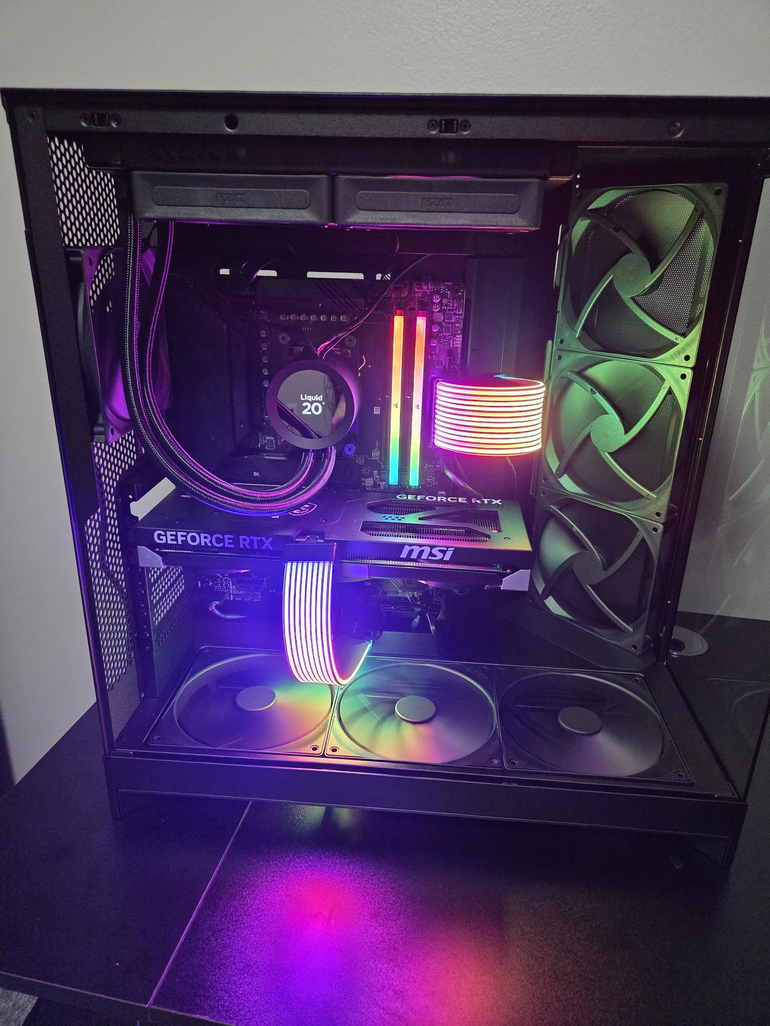 A custom gaming PC with RGB lighting inside a black case, featuring cooling fans, a graphics card labeled MSI and GeForce RTX, and internal components illuminated with multi-colored lights.