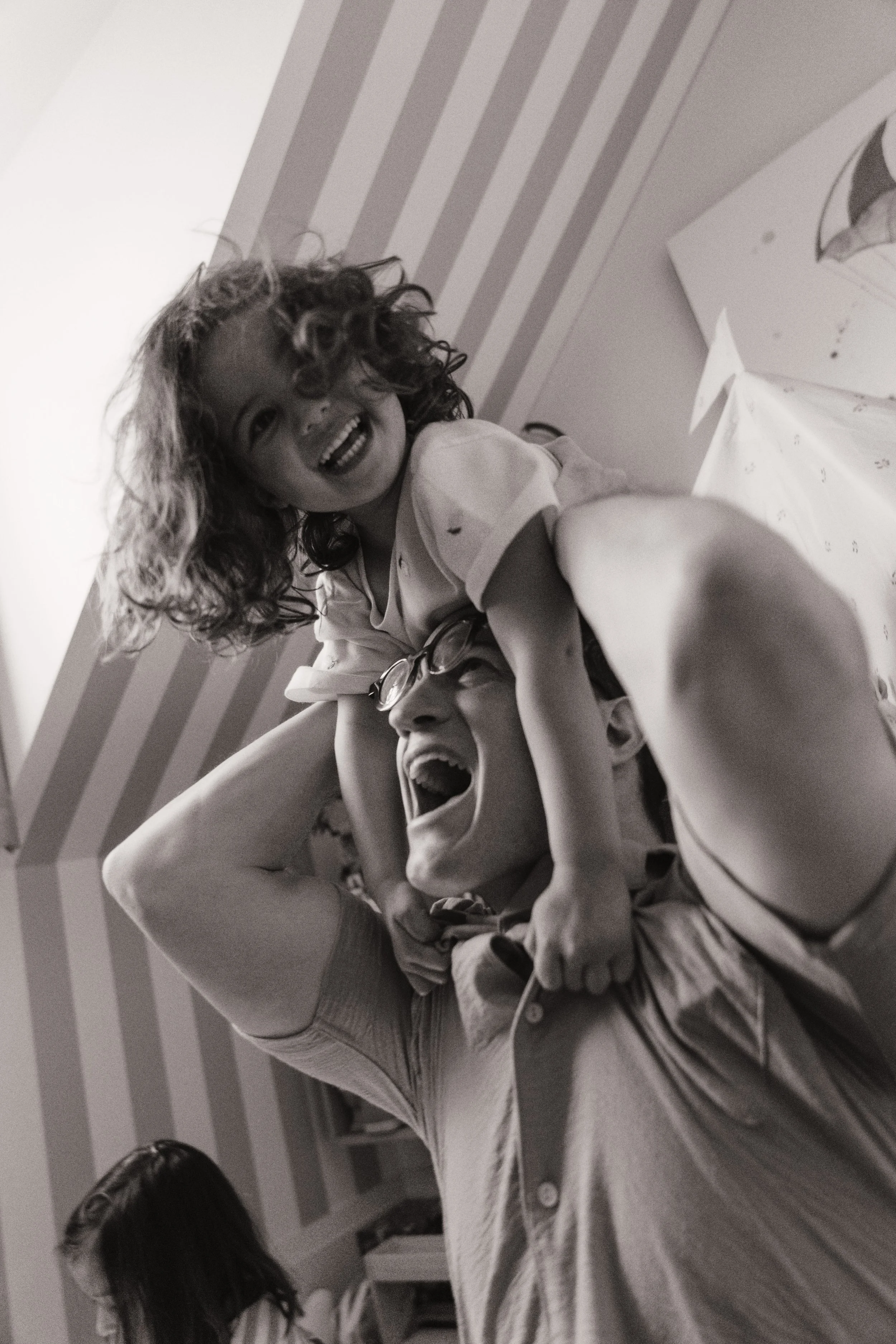 Black and white candid photo of a father carrying his daughter on his shoulders during an in-home family session.