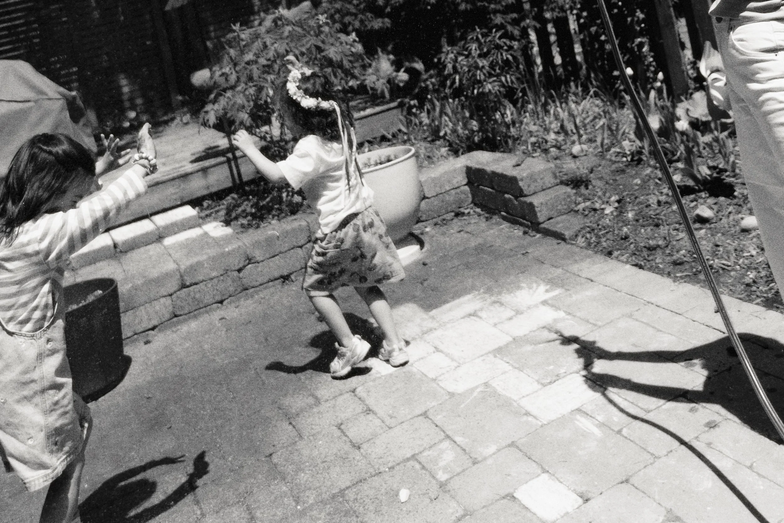 Black and white documentary-style family photo of children playing with water in the backyard.
