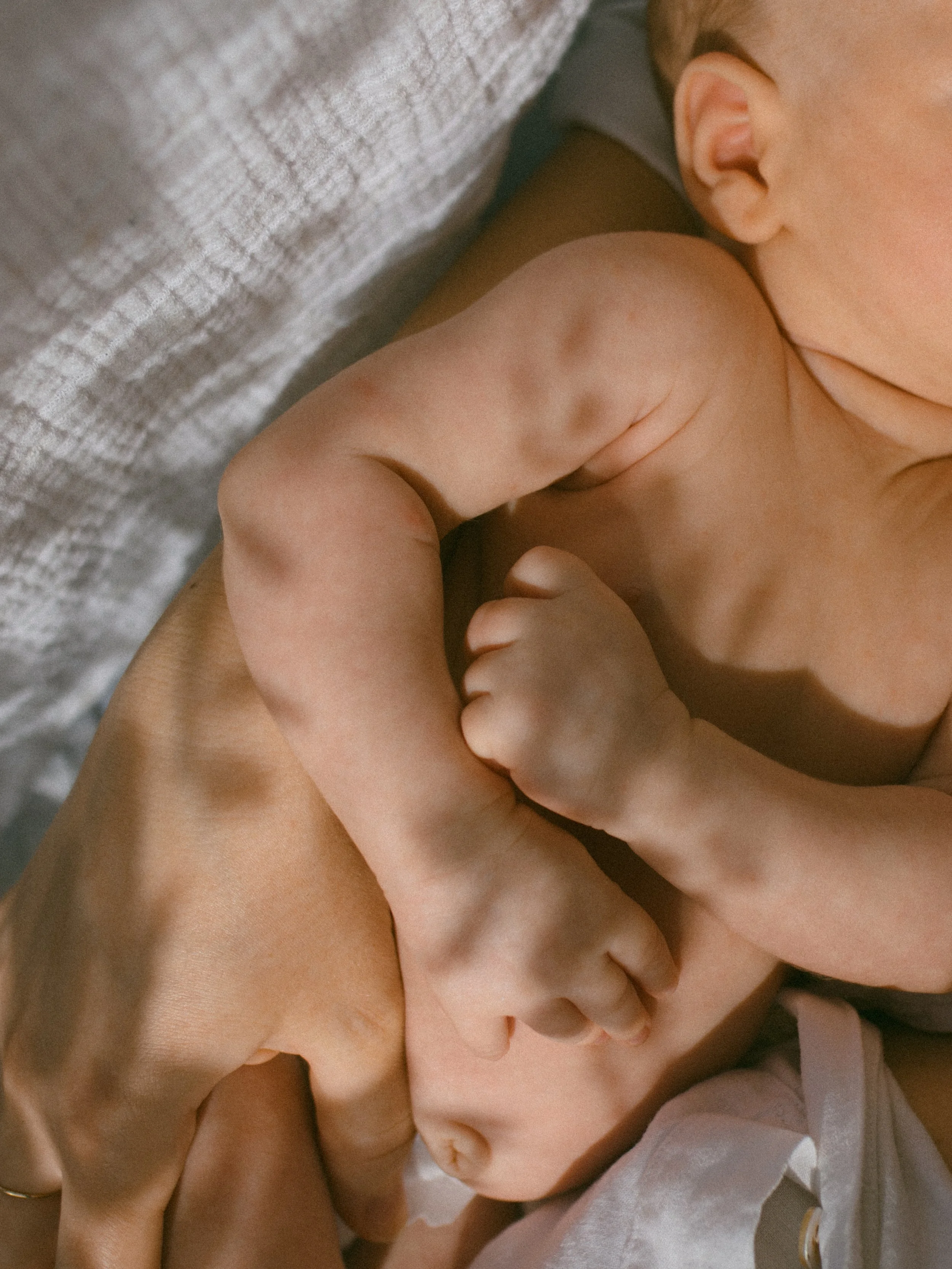 Close-up of a newborn baby sleeping peacefully, resting its head against an adult's chest, with soft natural lighting highlighting the baby's peaceful expression and delicate features.