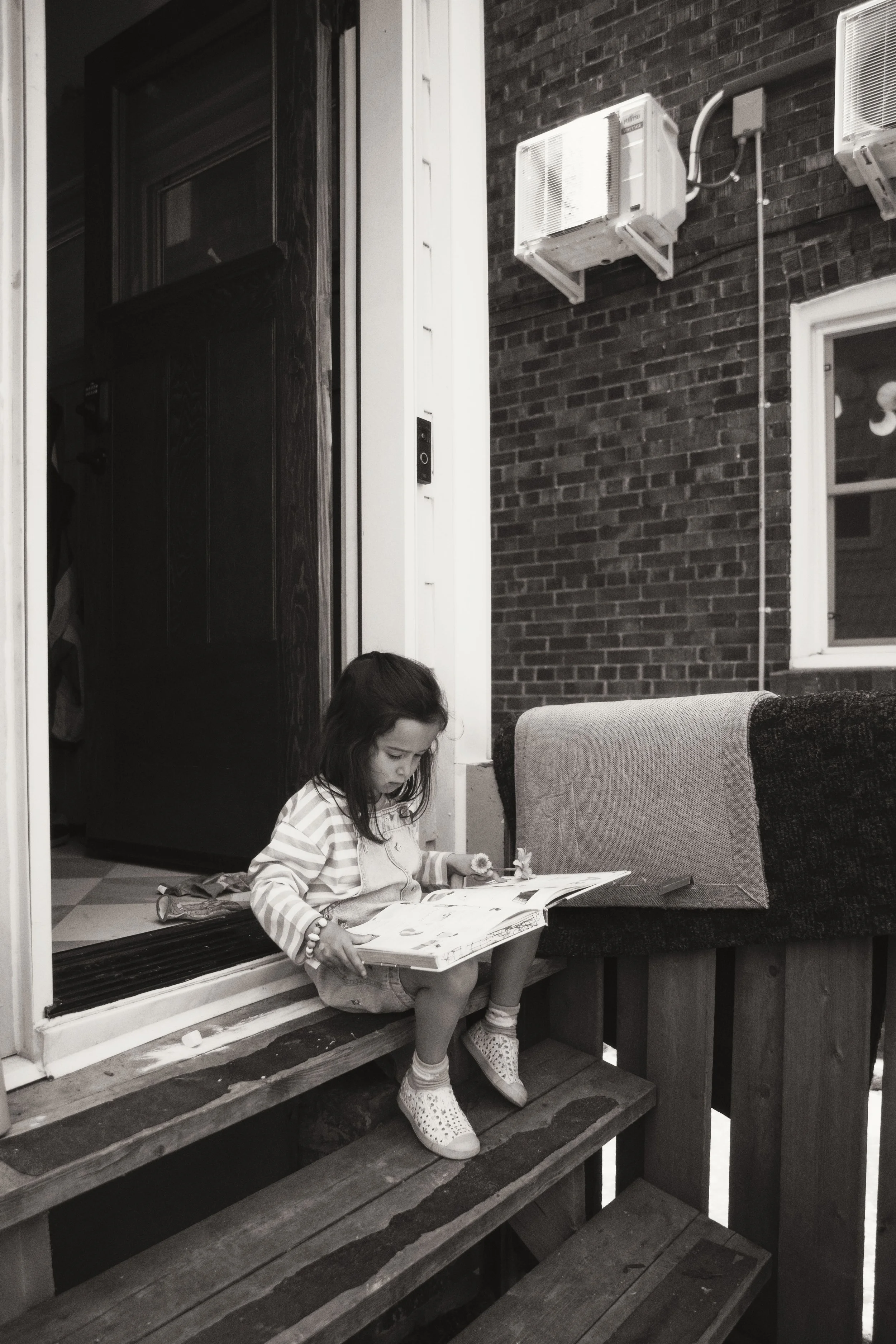 Black and white documentary photo of a child sitting on the back steps reading during an in-home family session.