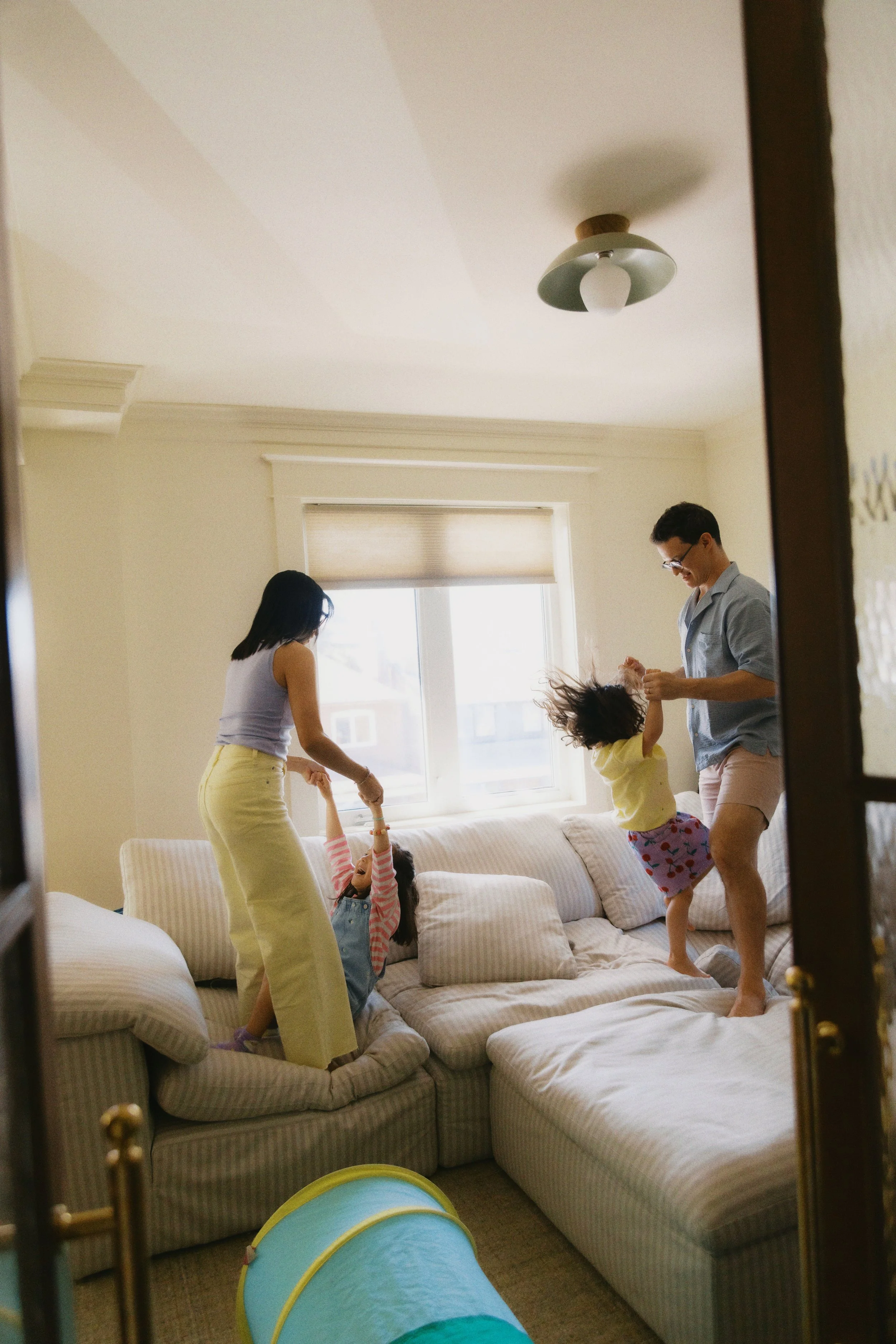 Candid family photo of parents playing with their children on the couch during an in-home family session.