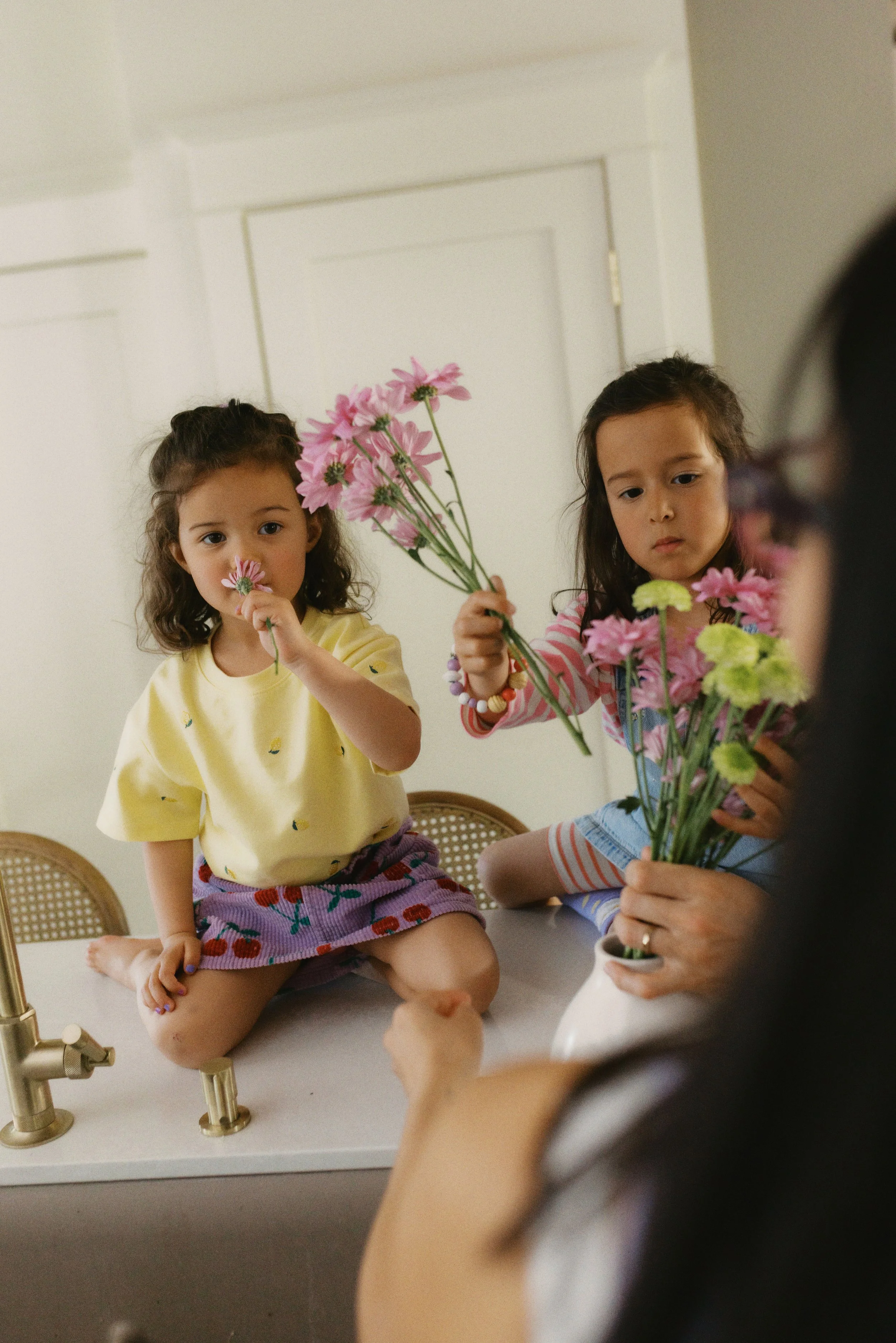 Candid family photo of two children arranging flowers on the kitchen counter during an in-home storytelling session.
