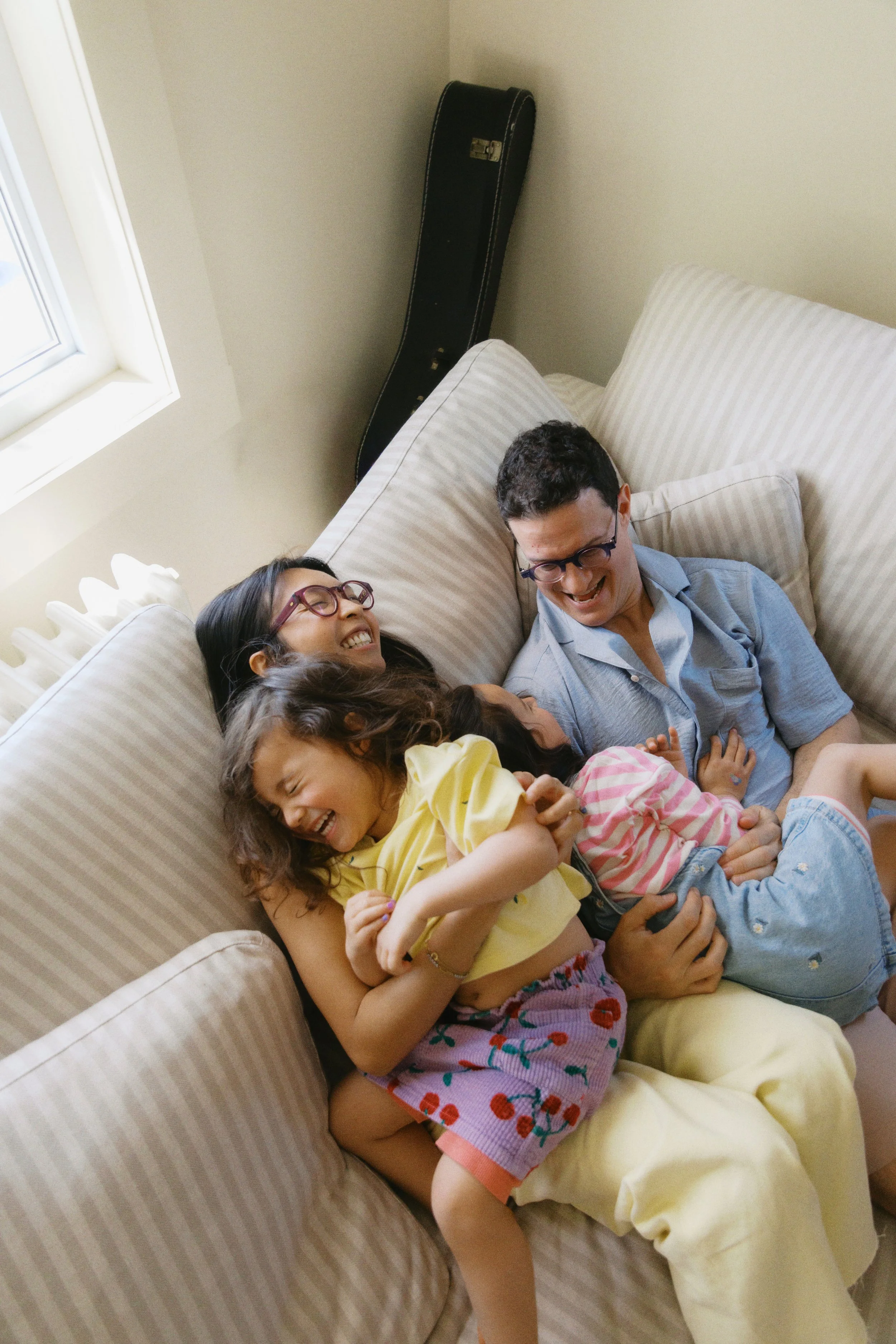 Natural in-home family photo of parents and children laughing together on the couch during a relaxed family session.